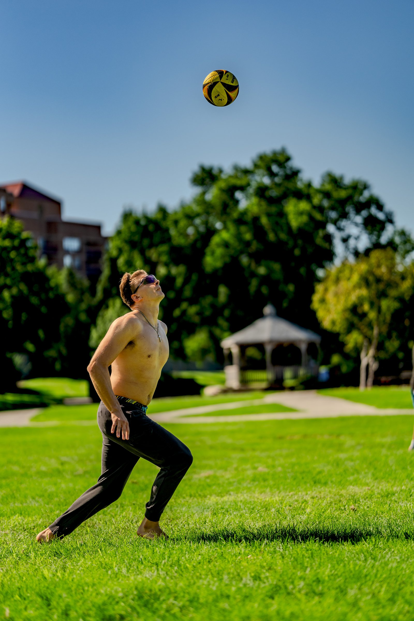 A player in black pants looks up at a volleyball in the air during a tournament on a sunny day.