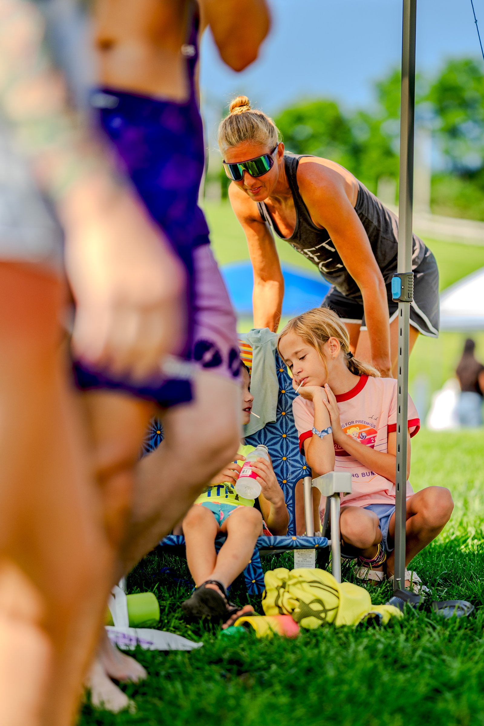 A player in a dark tank top and shorts watches children sitting in chairs, one holding a water bottle, at a tournament.