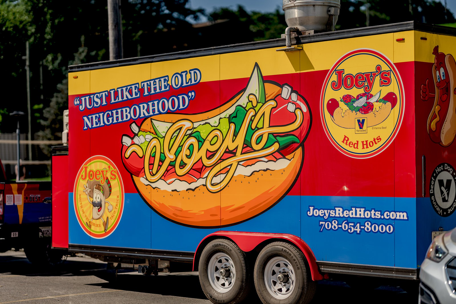 A food truck with "JUST LIKE THE OLD NEIGHBORHOOD" and "Joey's Red Hots" branding, featuring a large hot dog graphic and contact information.