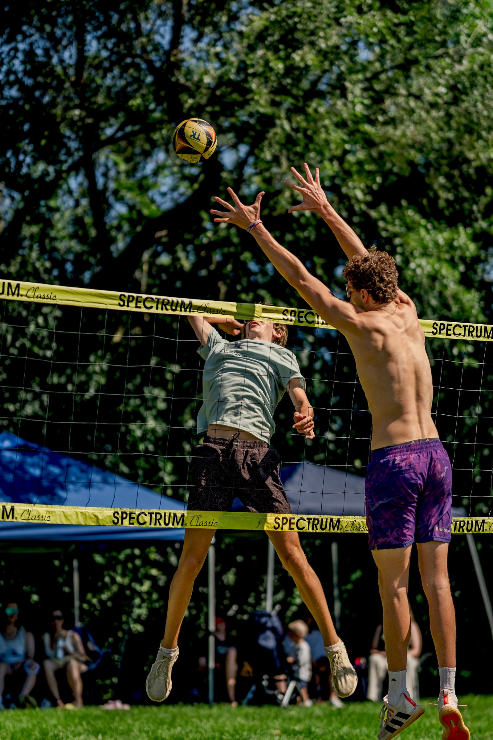 Two players jump near the net as a volleyball is in the air, with a yellow banner reading "SPECTRUM Classic" across the net.