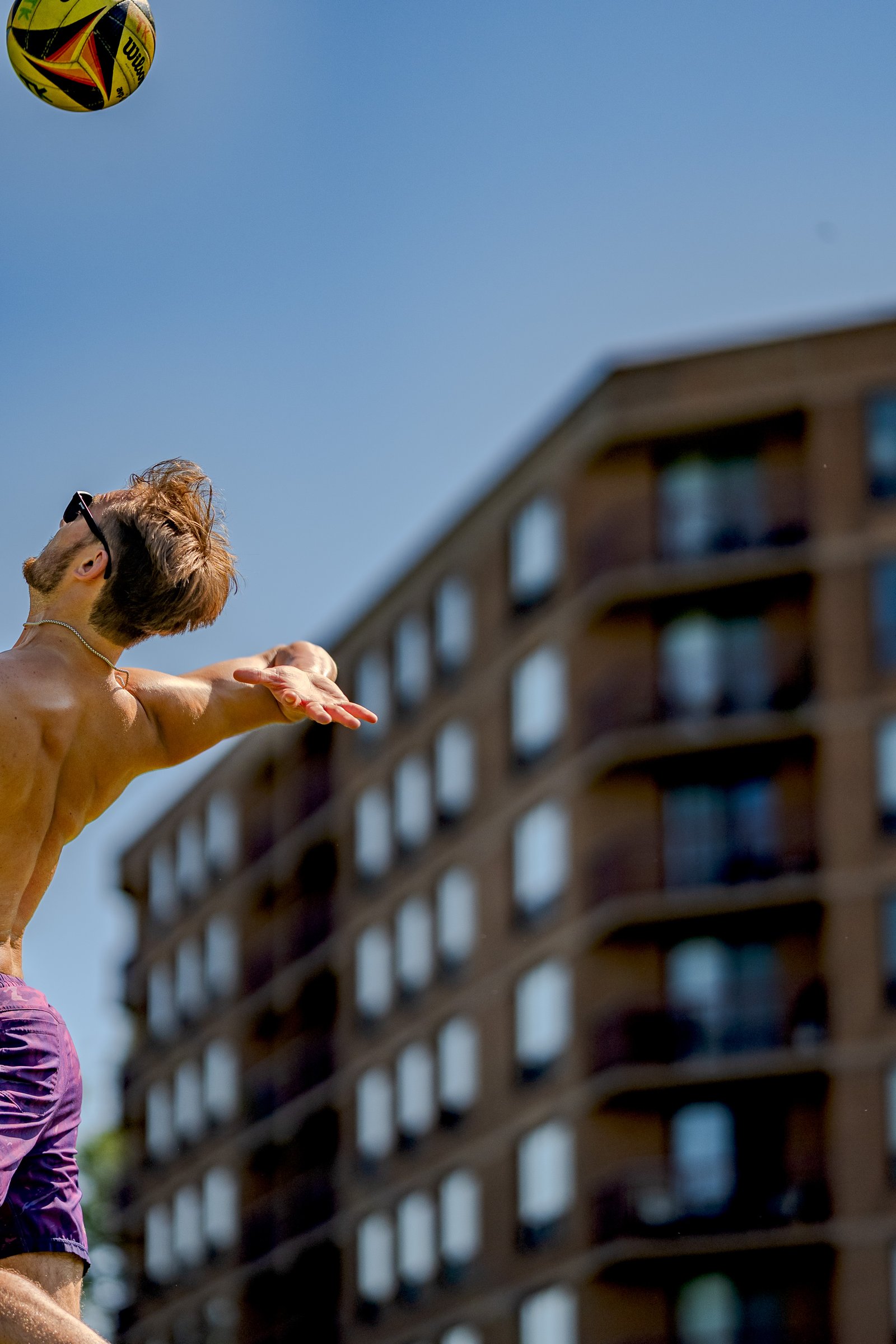 A player in purple shorts reaches for a volleyball against a building.