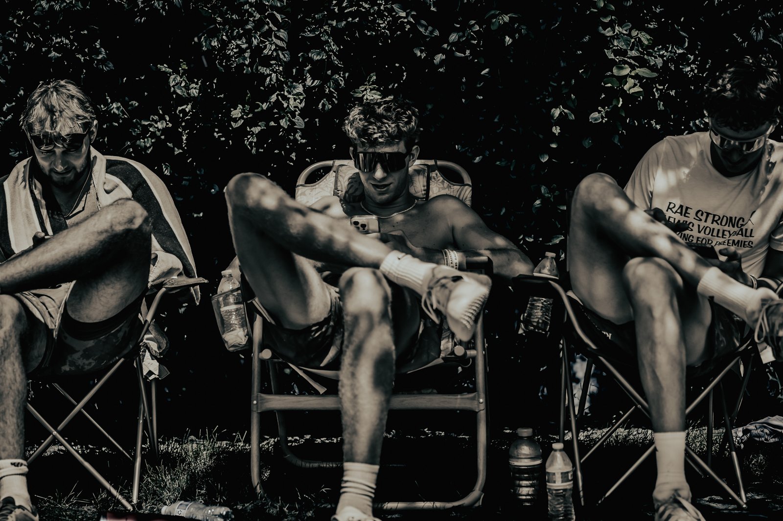 Three players in chairs, one in a white shirt with text, rest outdoors with a dark leafy background.