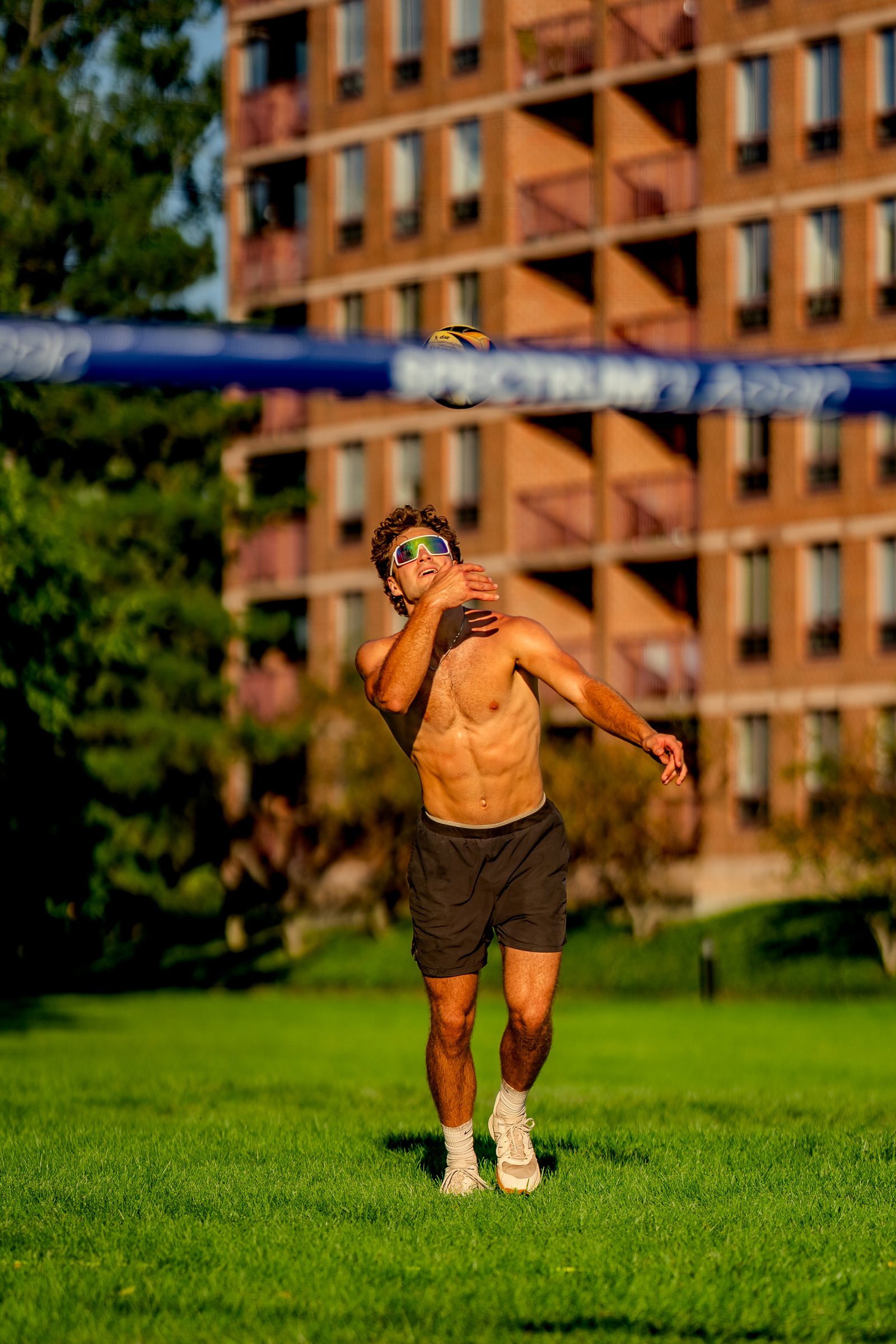 A player in black shorts prepares to hit a volleyball over the net on a sunny day.