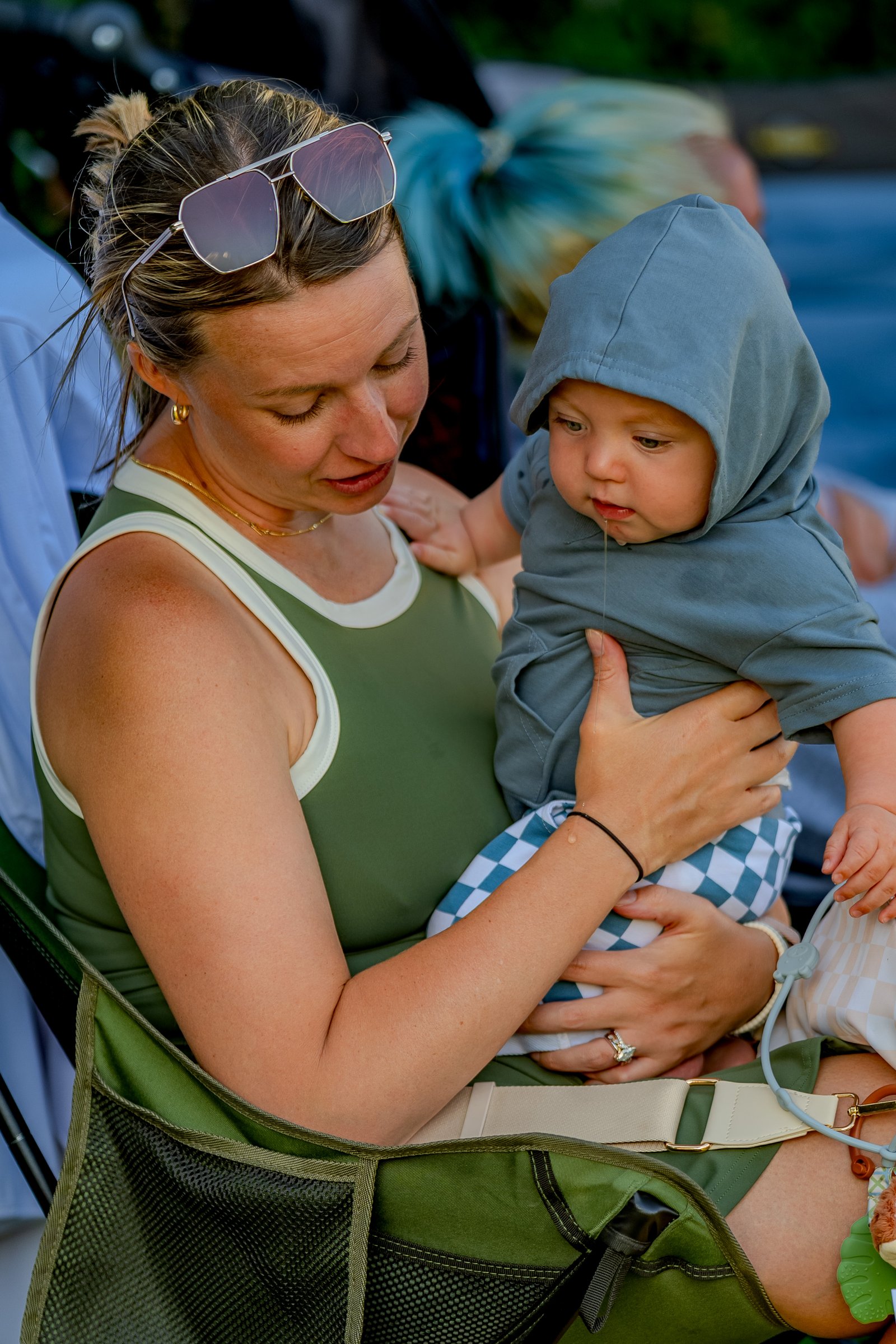 A player in a green top holds a baby in a grey hoodie while sitting in a chair at the tournament.
