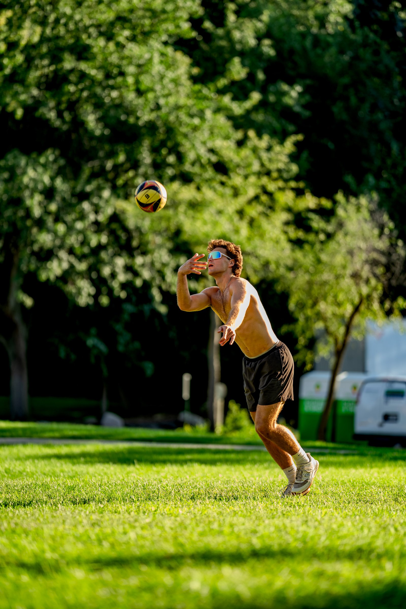 A player in black shorts sets a volleyball in a park during a tournament.