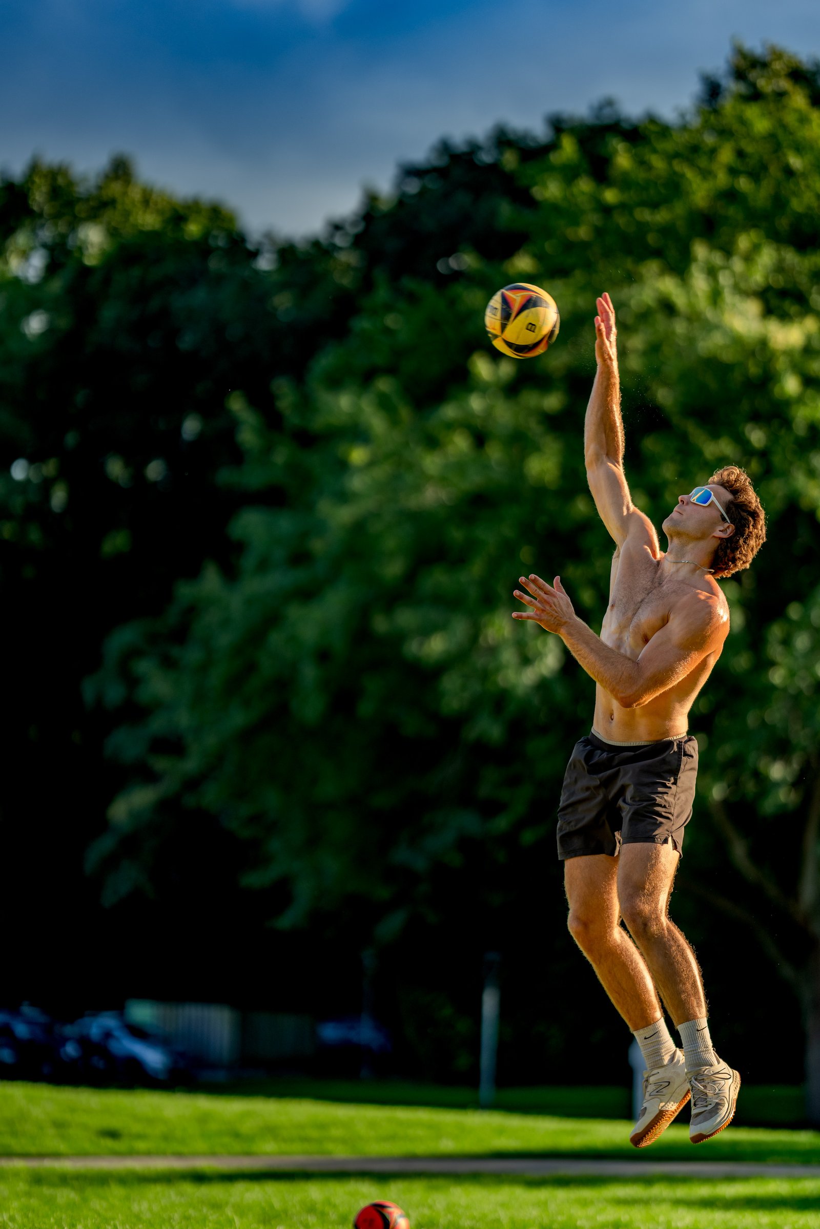 A player in black shorts jumps to hit a volleyball against a green tree background.