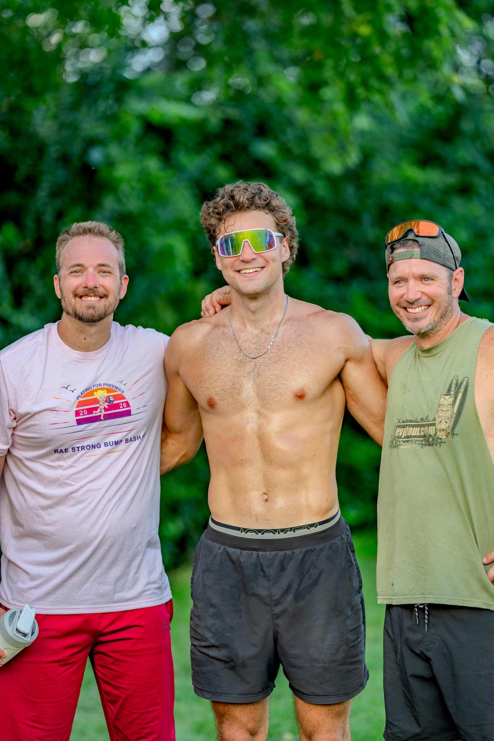 Three smiling players pose for a photo at the Bump Bash tournament. One player wears a pink shirt, another a green tank top, and the third is shirtless.