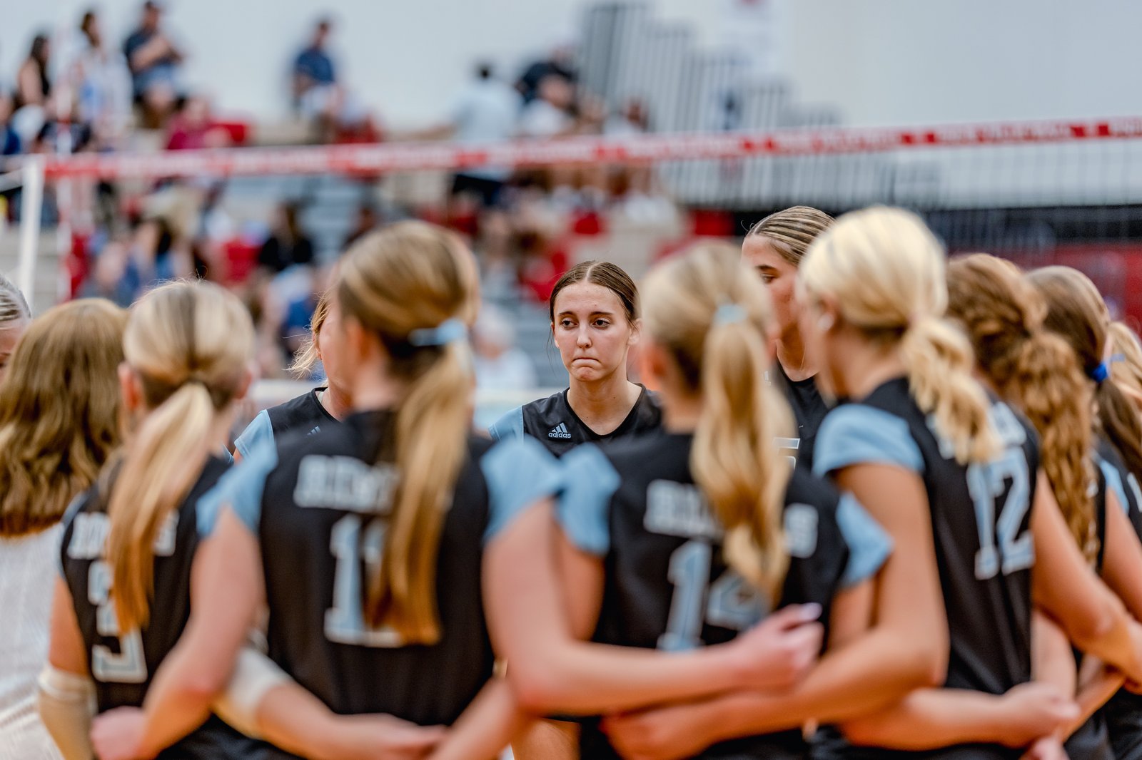 Players in black and light blue jerseys huddle together, one player looking forward with a concerned expression.