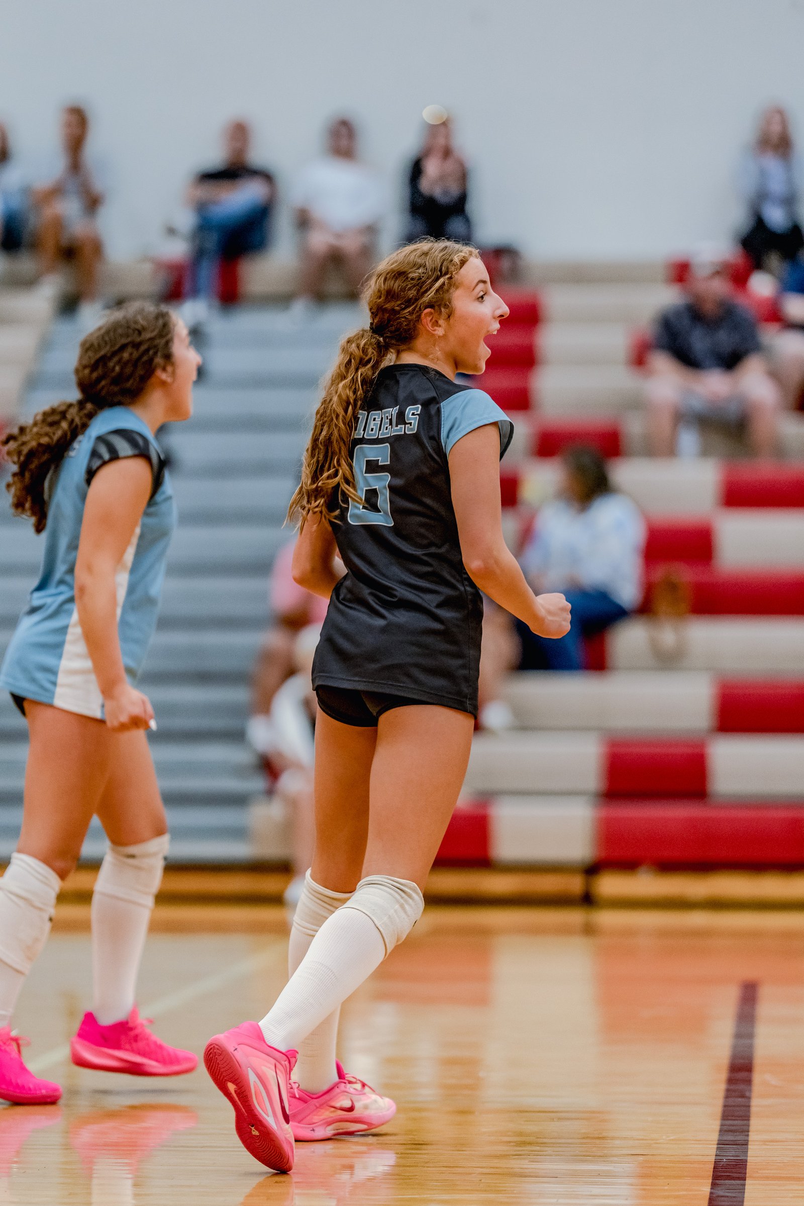 A player in a black jersey with light blue accents and number 6 yells on the court, with a teammate in a light blue jersey behind her.