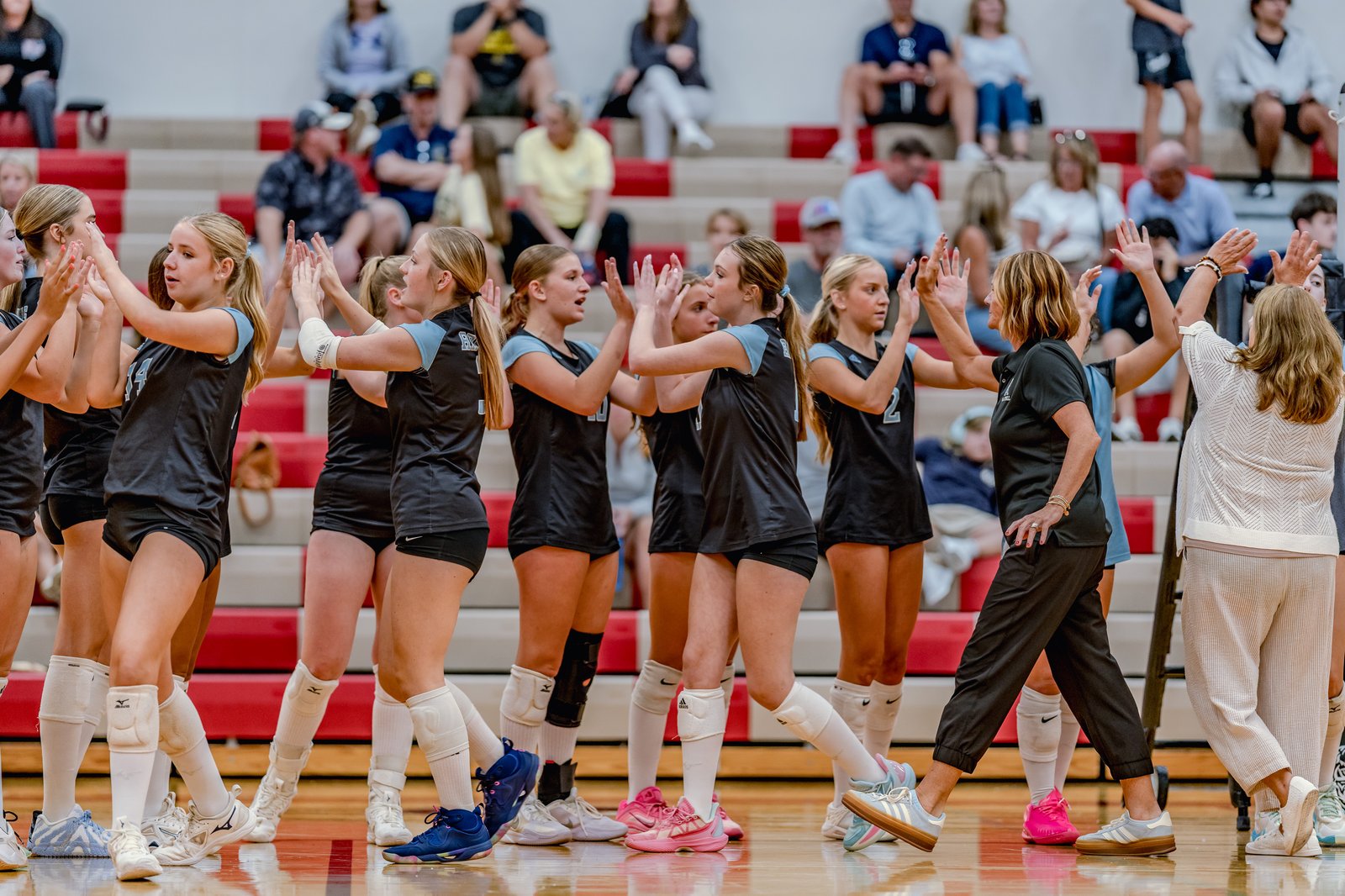 Players in black and light blue jerseys high-five on the court during a game.