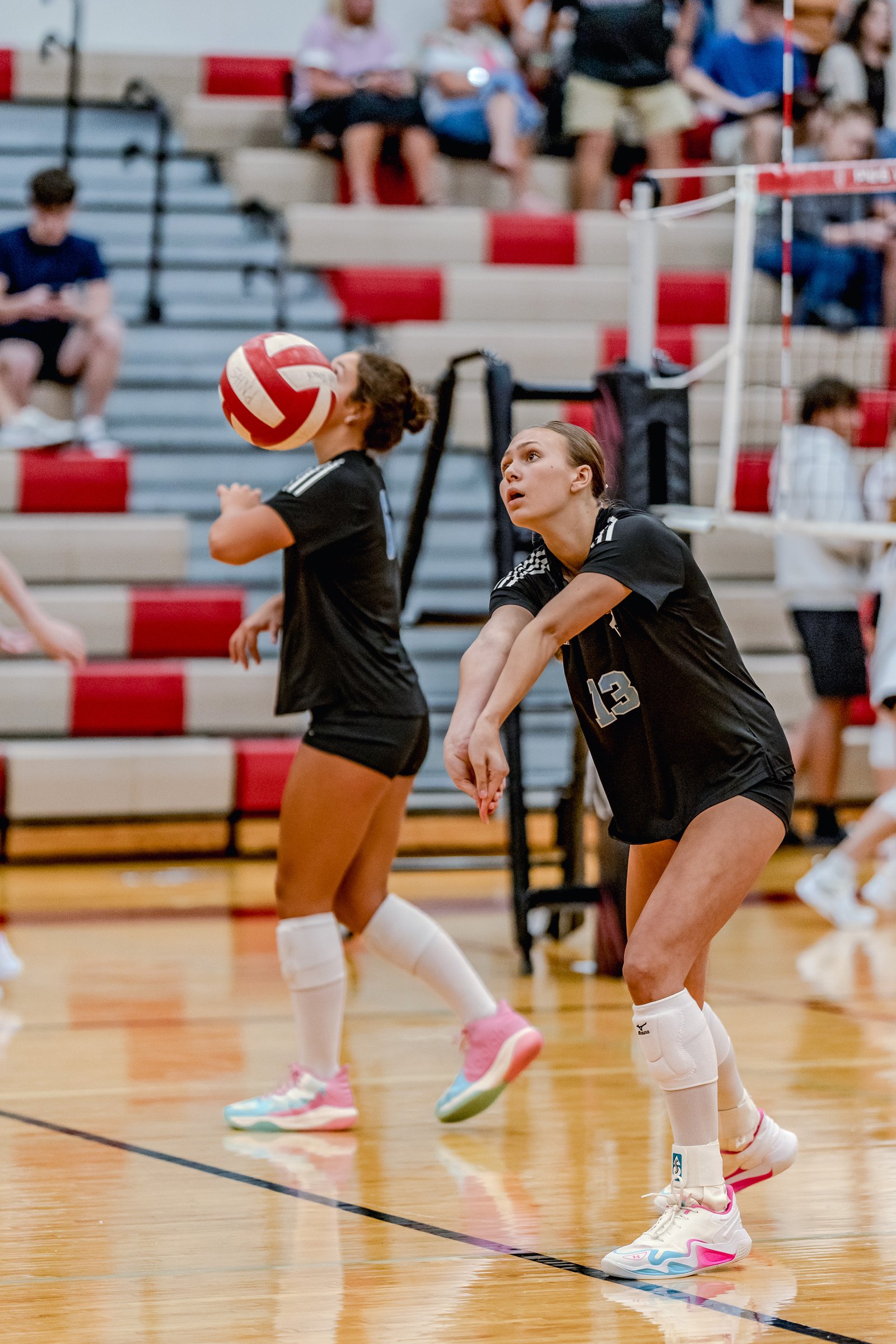 Two players in black tops and white socks play volleyball, one with a ball near her face, the other in a ready stance.