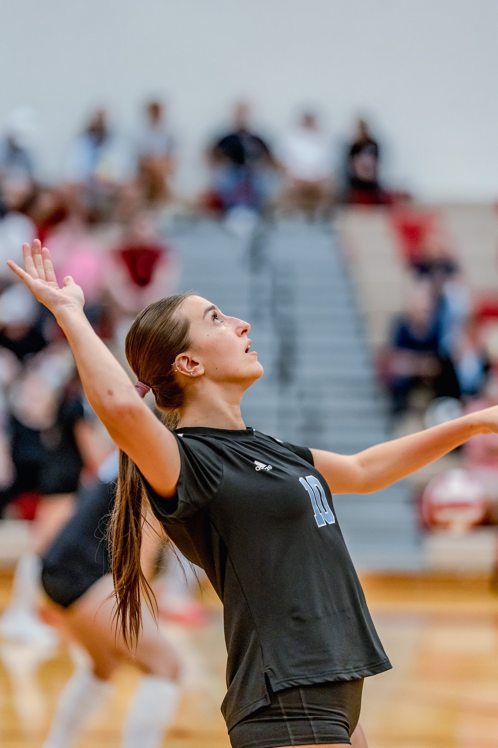 A player in a black jersey with light blue number 10 sets the ball during a volleyball game.