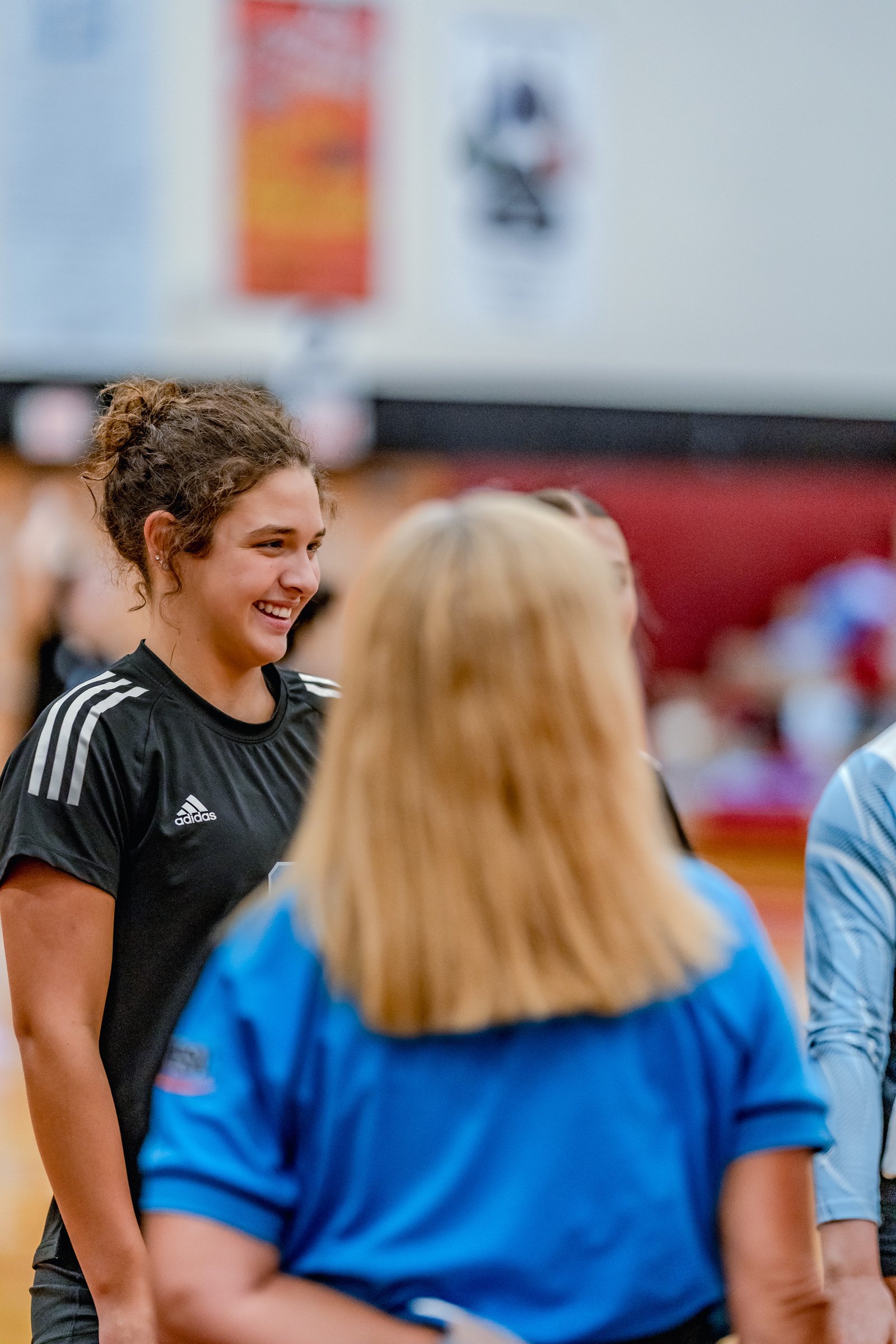 A player in a black top smiles while talking to a player in a blue top during a volleyball game.