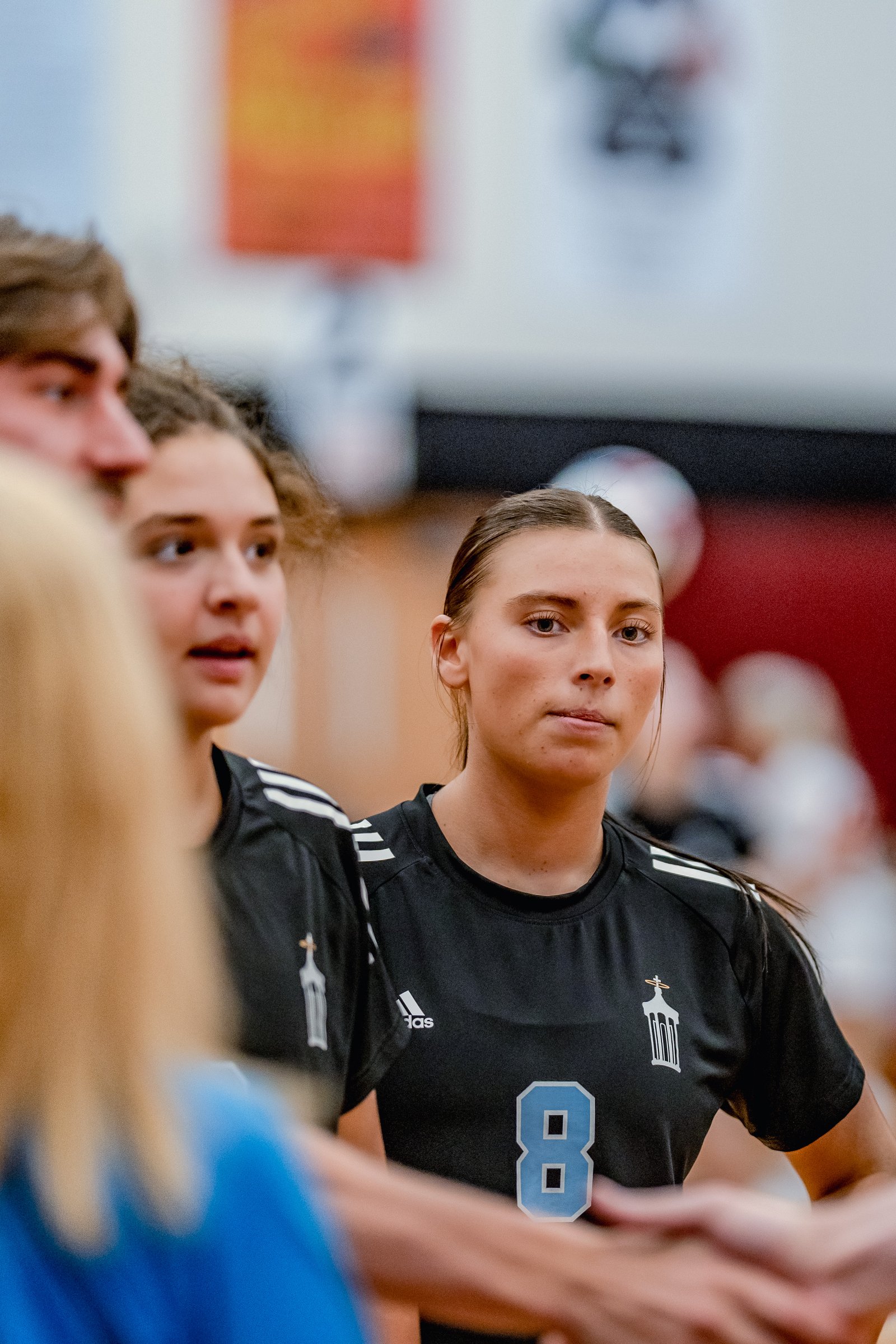 A player in a black jersey with white stripes and number 8 looks intently during a volleyball game.