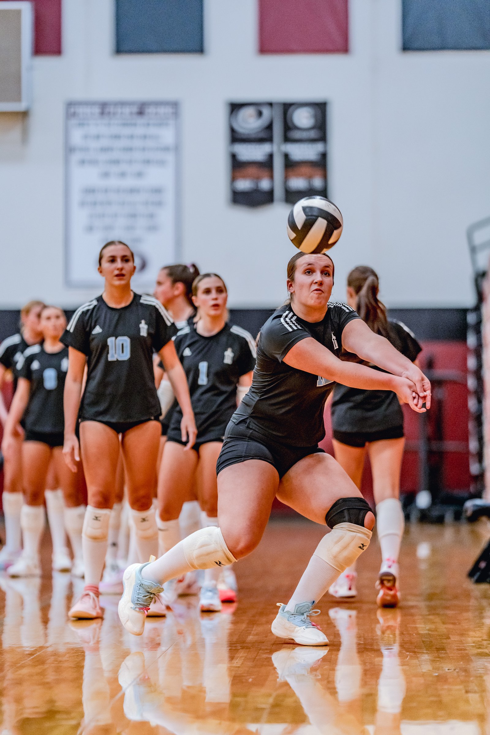 A player in a black top with number 10 passes a volleyball during a game, with teammates in black behind her.