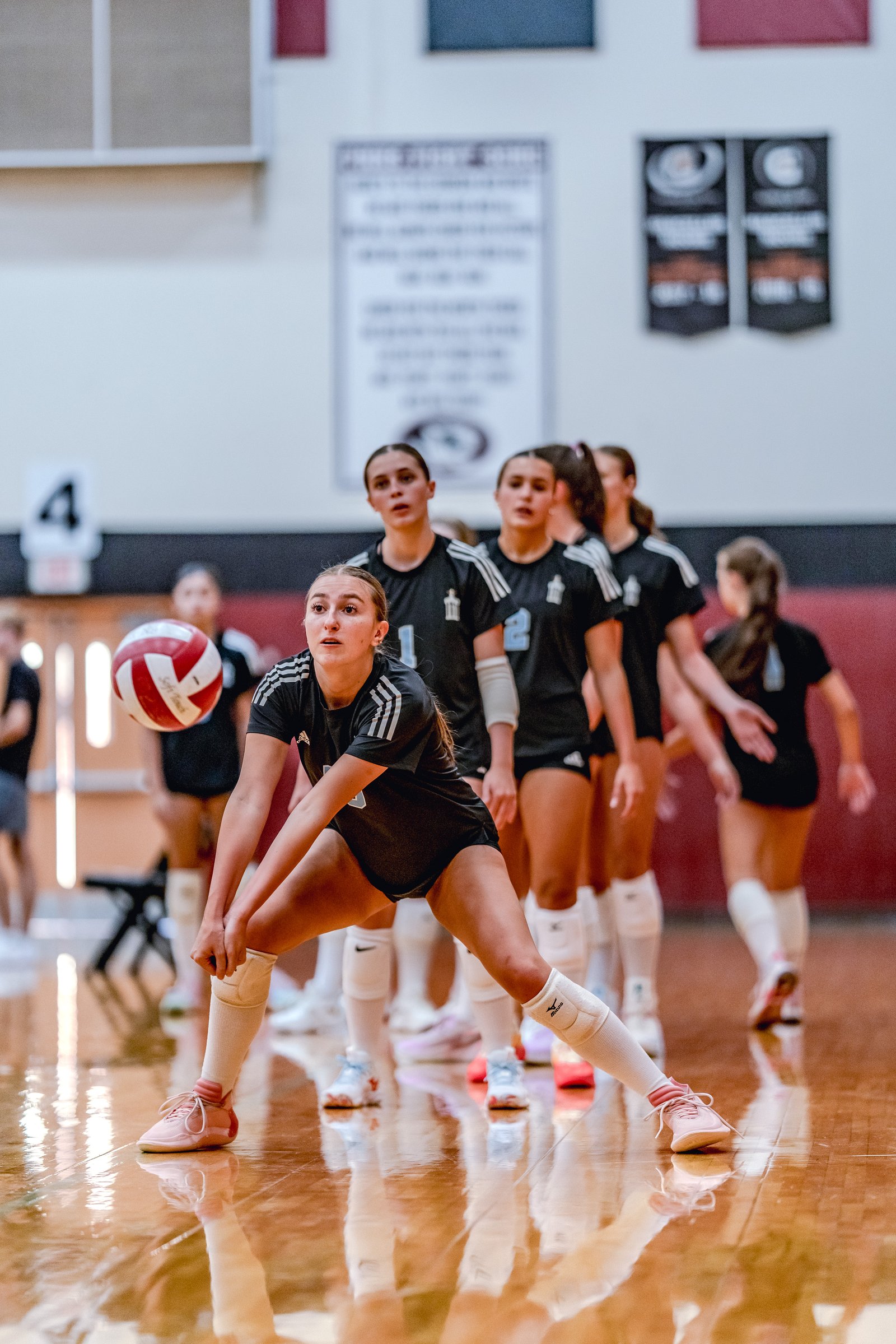 A player in black with white stripes receives a volleyball during a game, with teammates in black behind her.