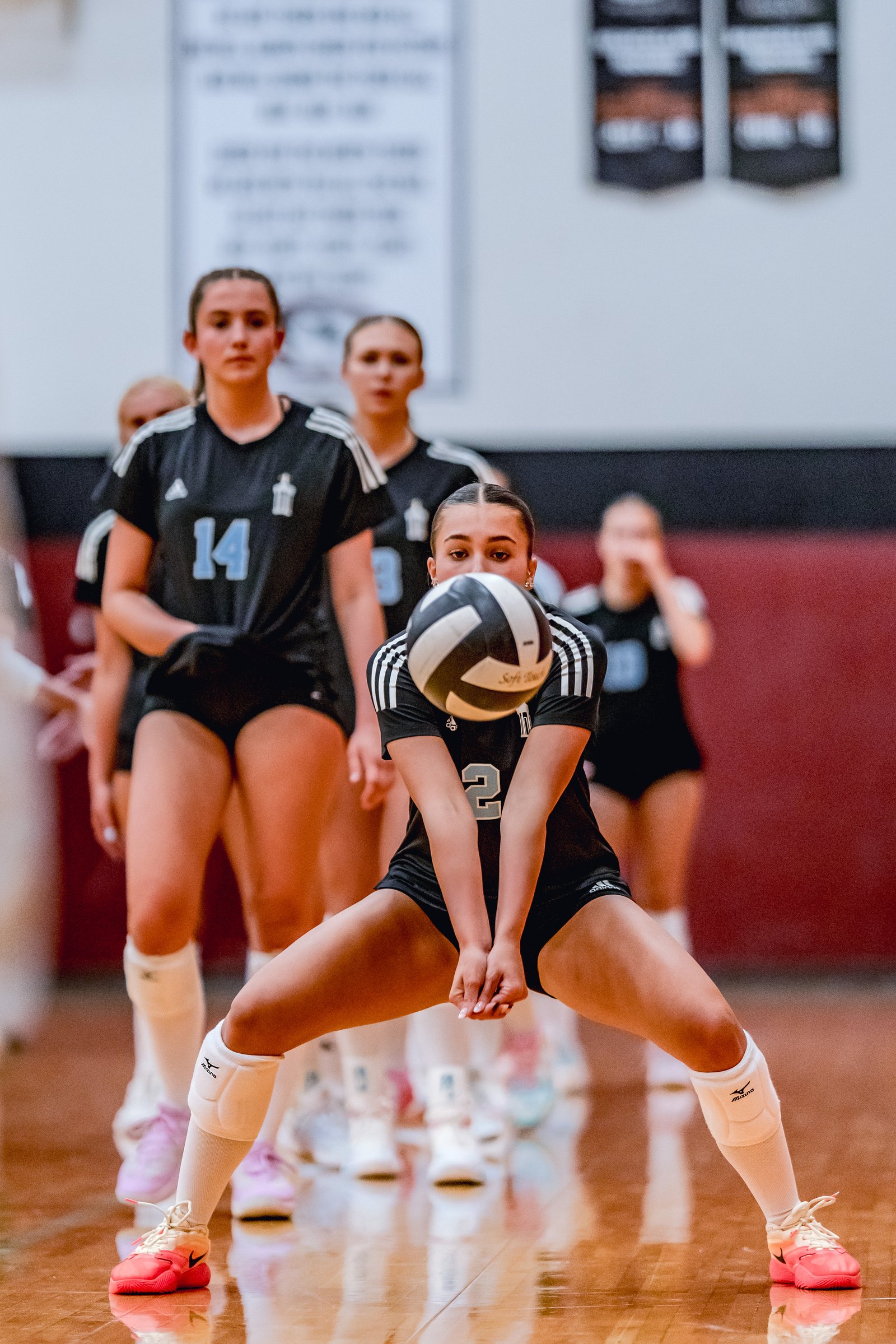 A player in black with jersey number 2 prepares to pass a volleyball, with teammates in black behind her on the court.