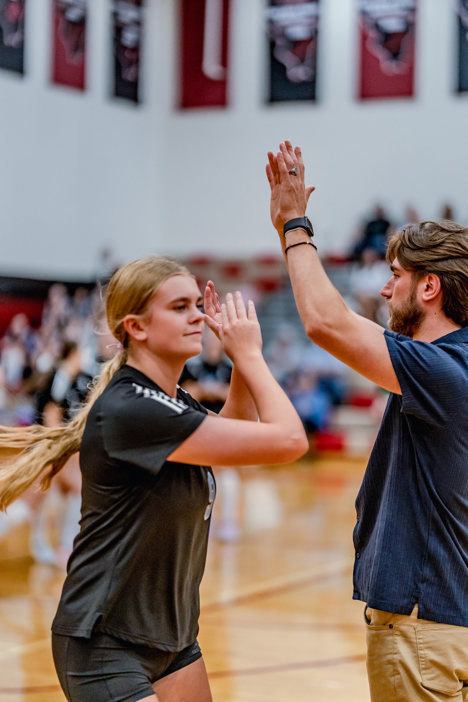 A player in a black top high-fives a coach in a blue shirt on the court.