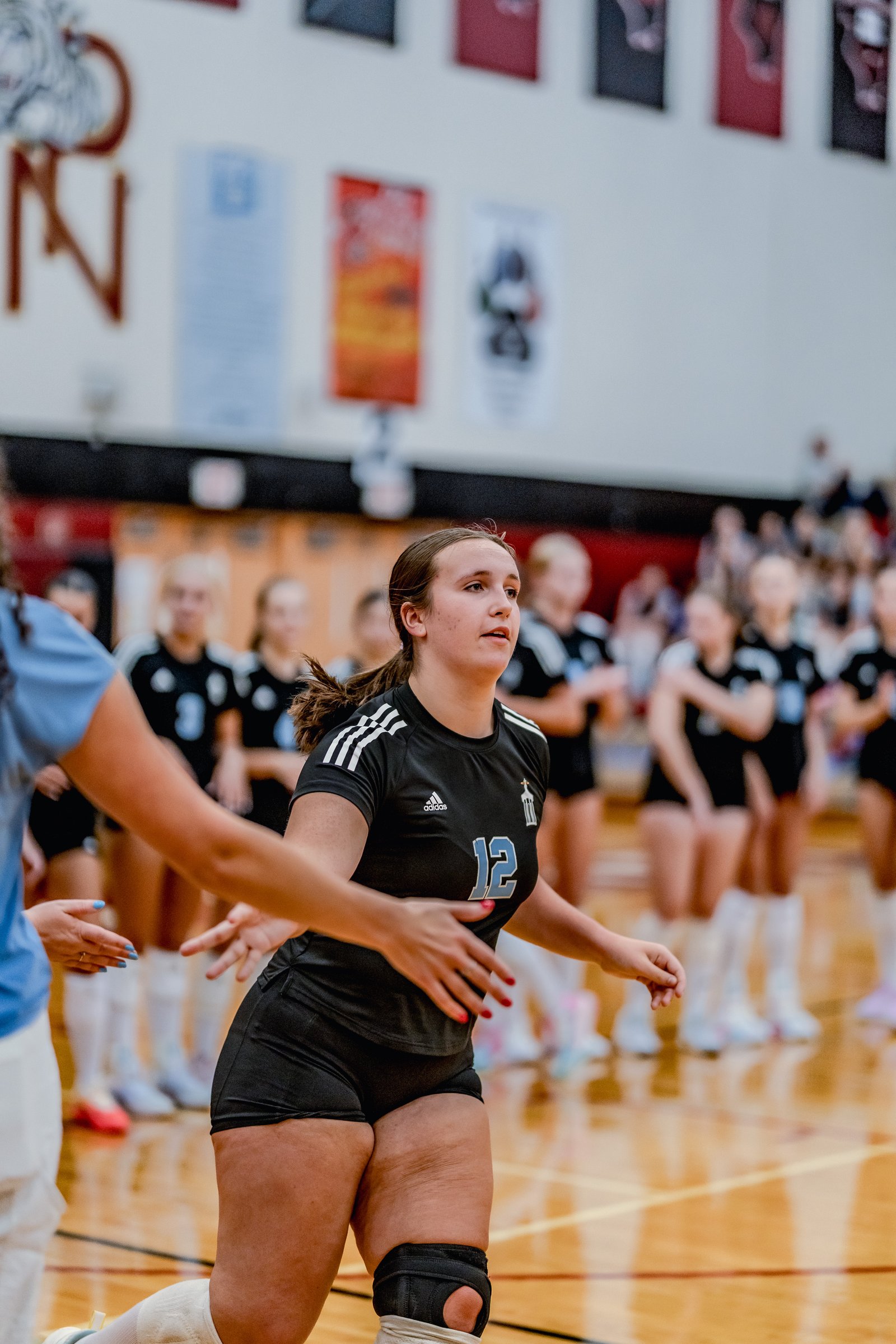 A player in a black jersey with number 12 moves on the court with teammates in black jerseys behind her.