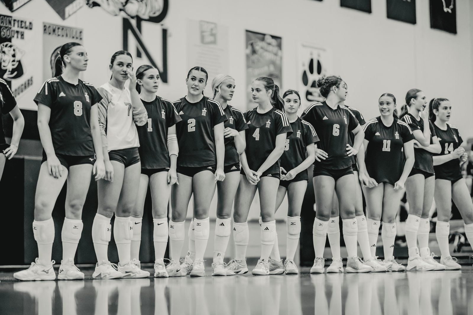 Players in black and white jerseys stand on a court, some looking away, with jersey numbers 8, 7, 1, 2, 4, 6, 11, and 14 visible.