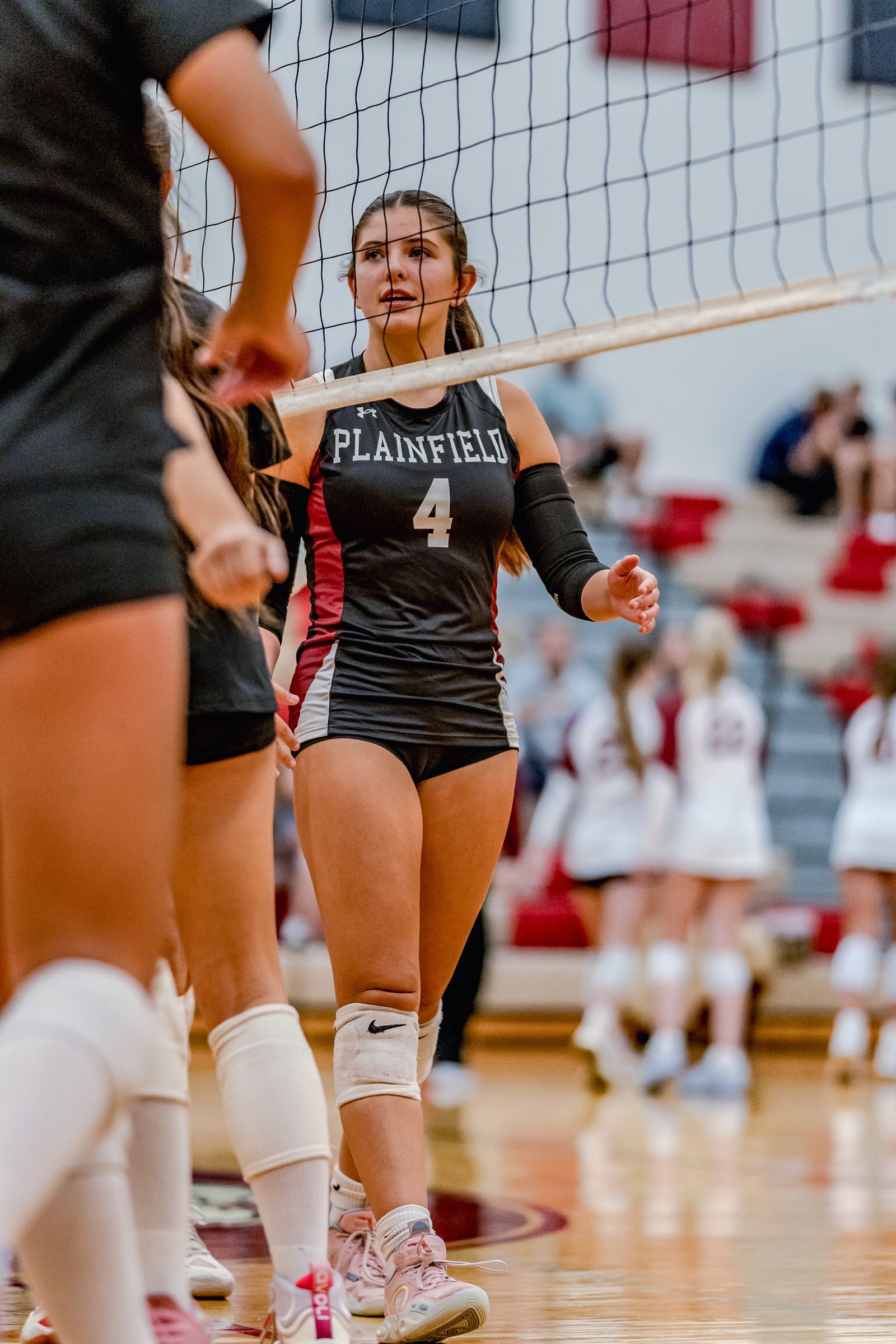 A player in a black and maroon jersey with number 4 on the court during a volleyball game.