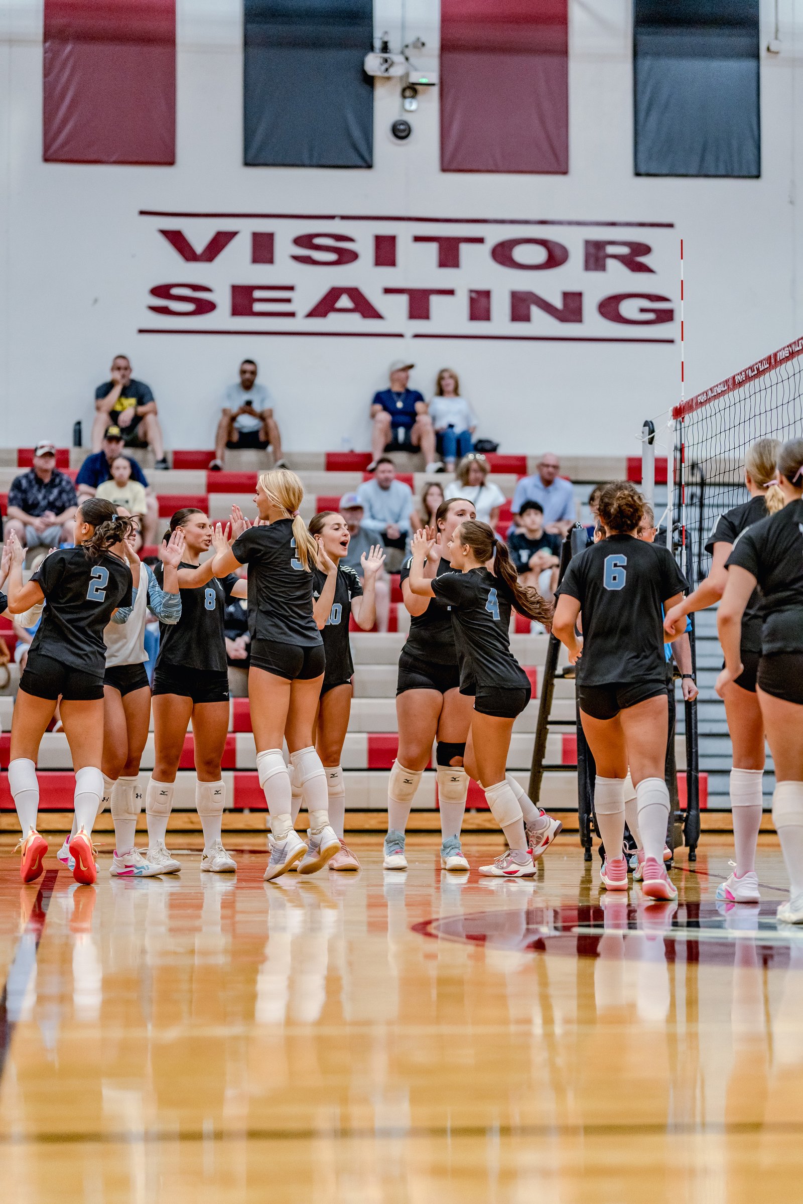 Players in black and white uniforms high-five on the court during a volleyball game, with spectators in the background.