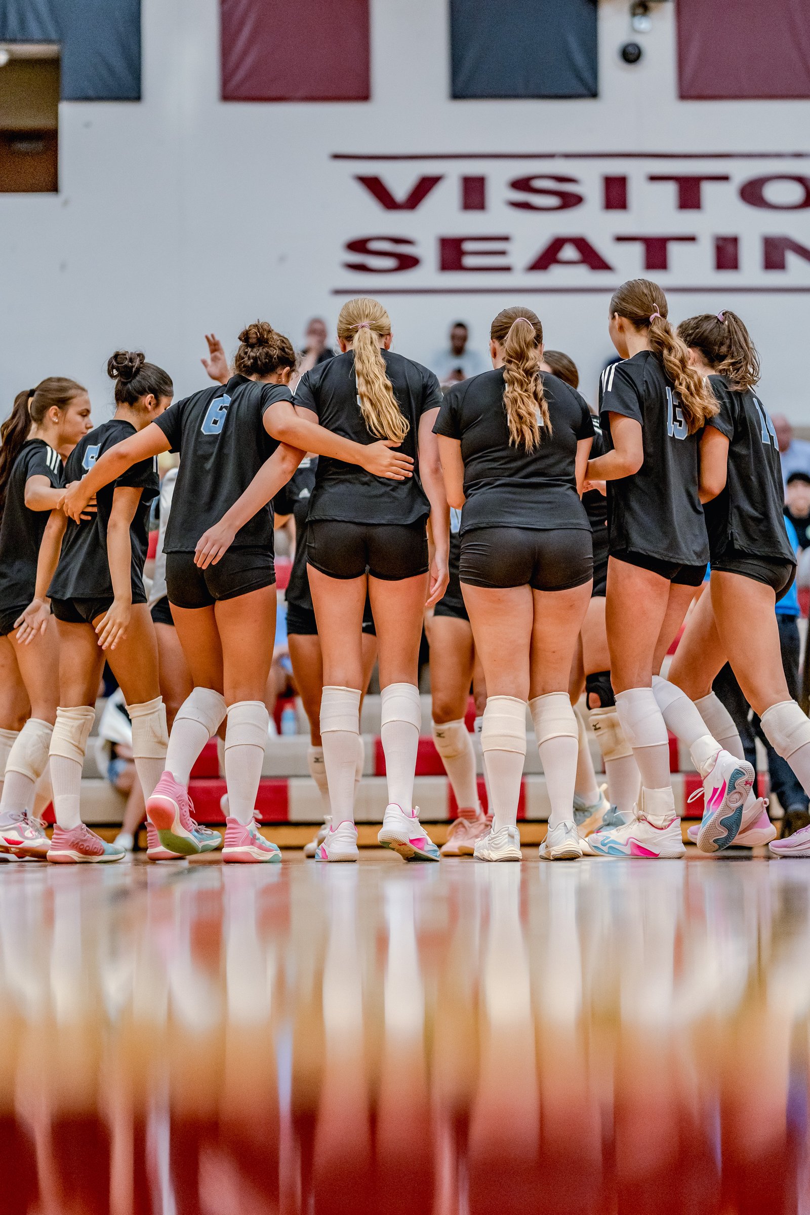 Players in black jerseys huddle together on the court, with visible jersey numbers 6, 15, and 14.