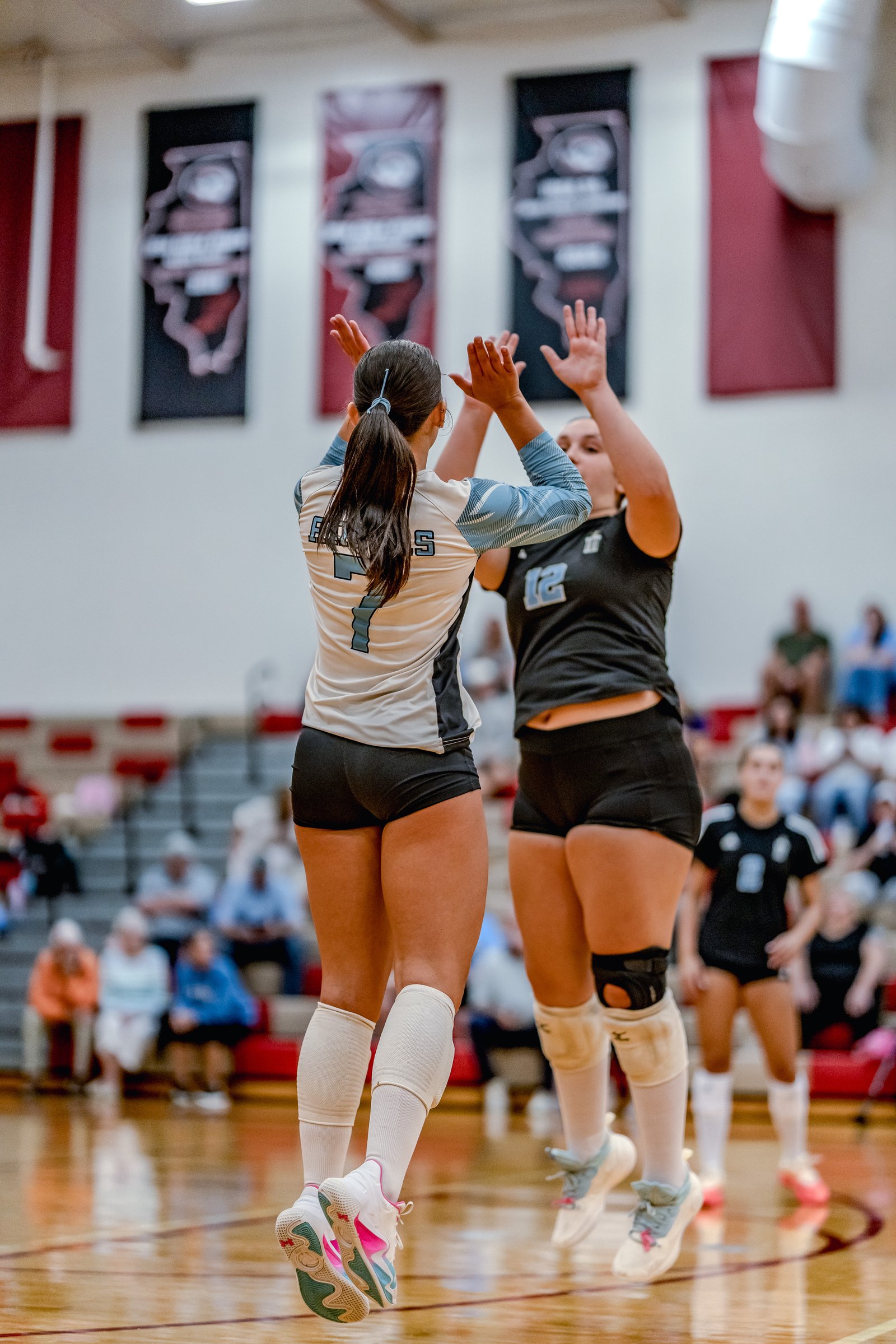 Two players in light blue and black jerseys high-five during a volleyball game.