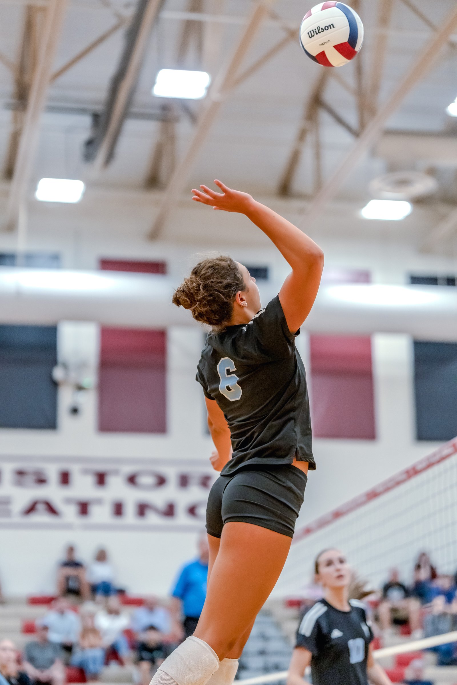 A player in a black jersey with number 6 jumps to hit a volleyball over the net, with another player in black watching.