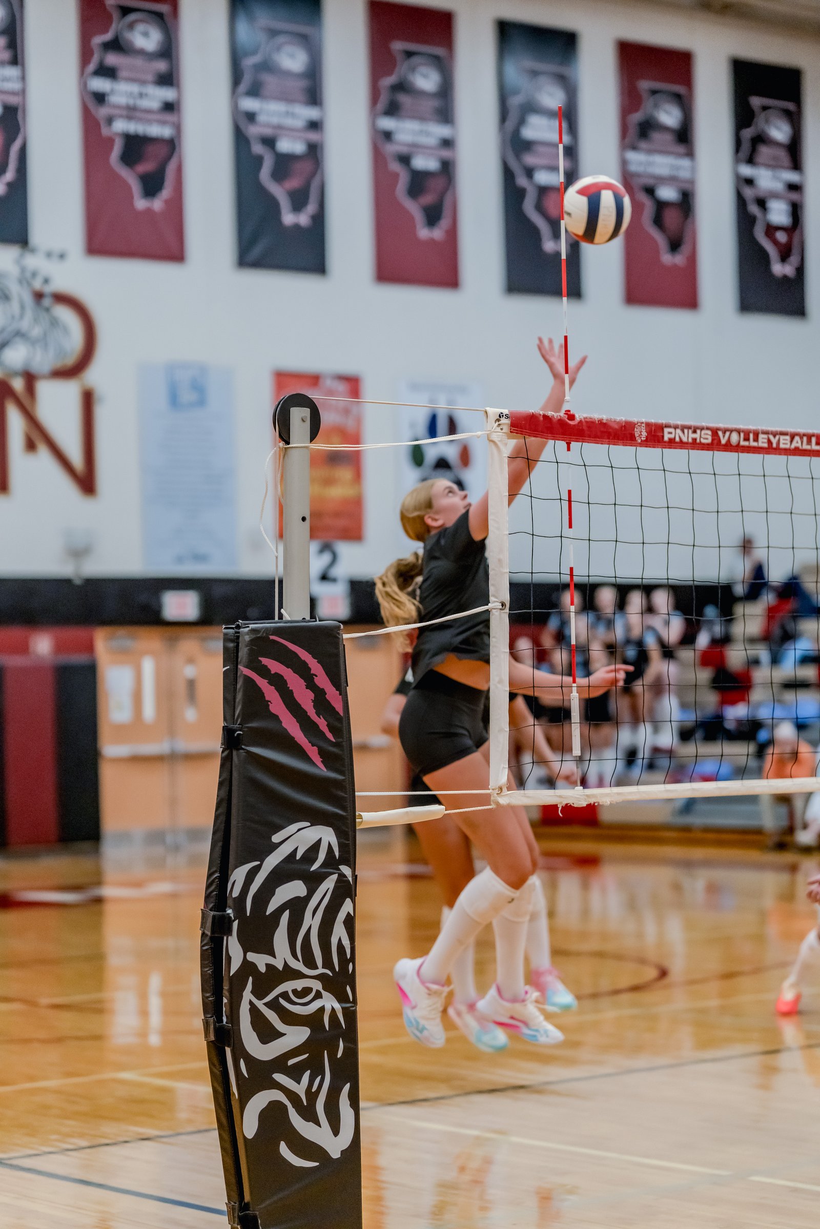 A player in black jumps to hit a volleyball over the net during a game.