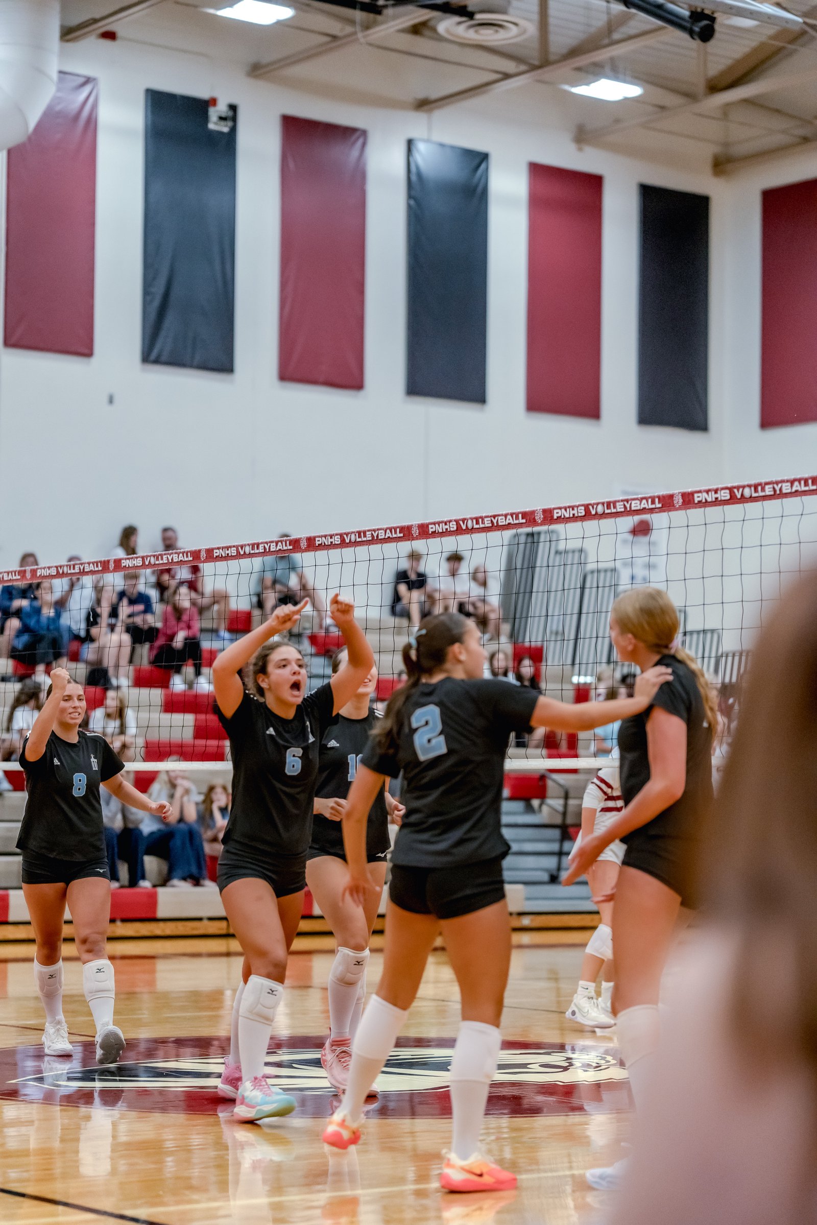 Players in black jerseys celebrate on the court during a volleyball game, with one player in jersey number 6 and another in number 8.