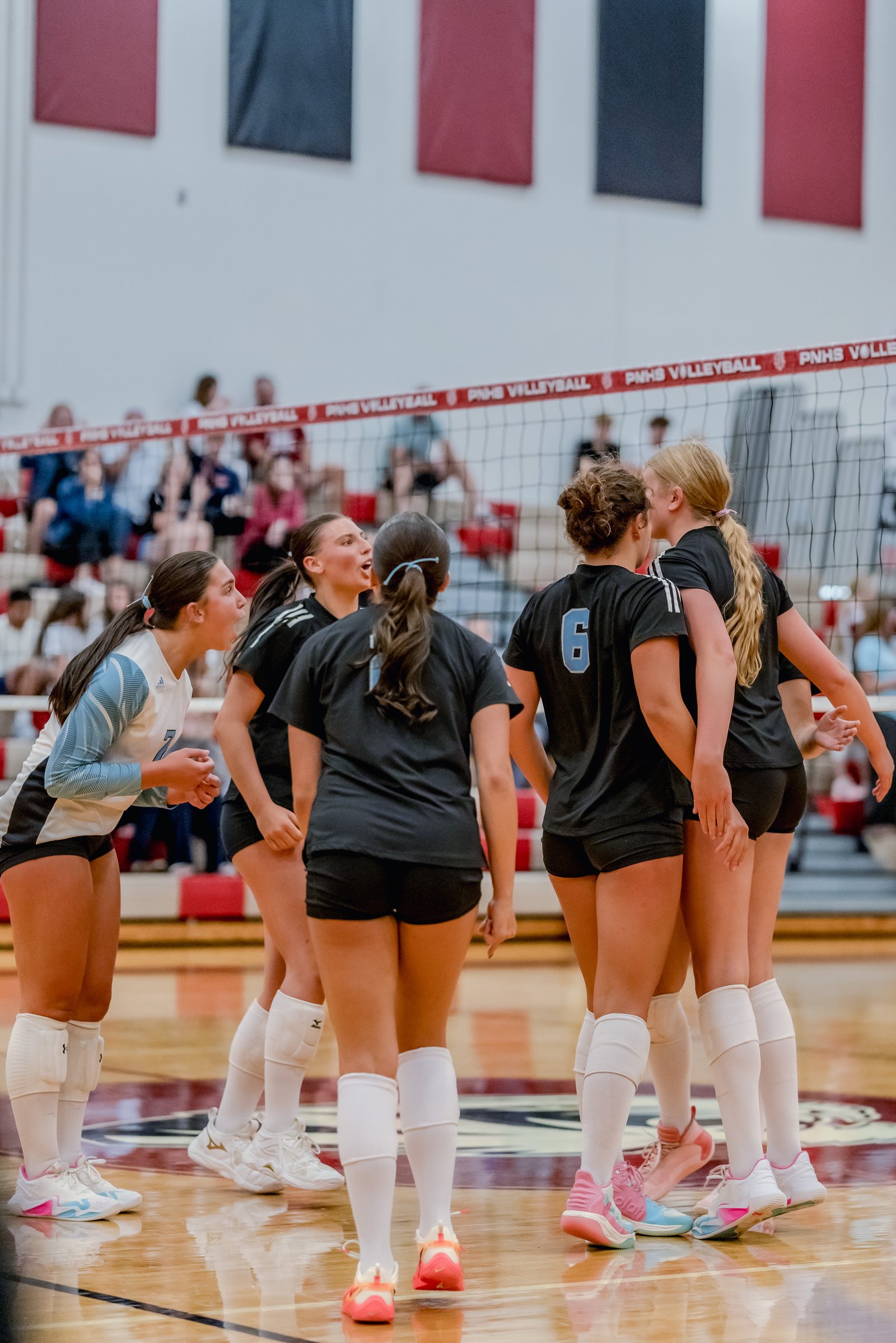 Players in black and light blue jerseys huddle on the court during a volleyball game.
