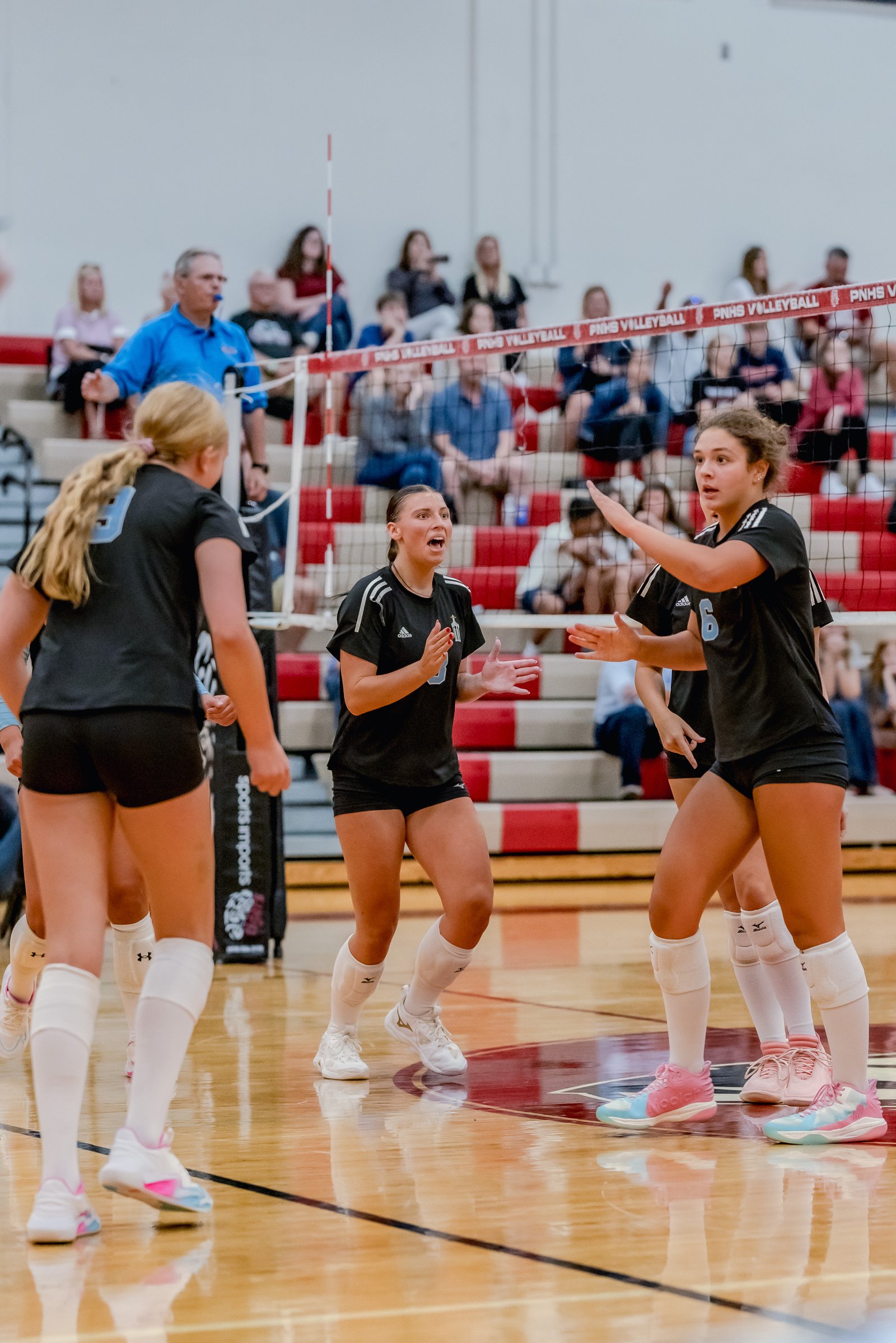 Players in black uniforms with light blue numbers celebrate on the court during a volleyball game.
