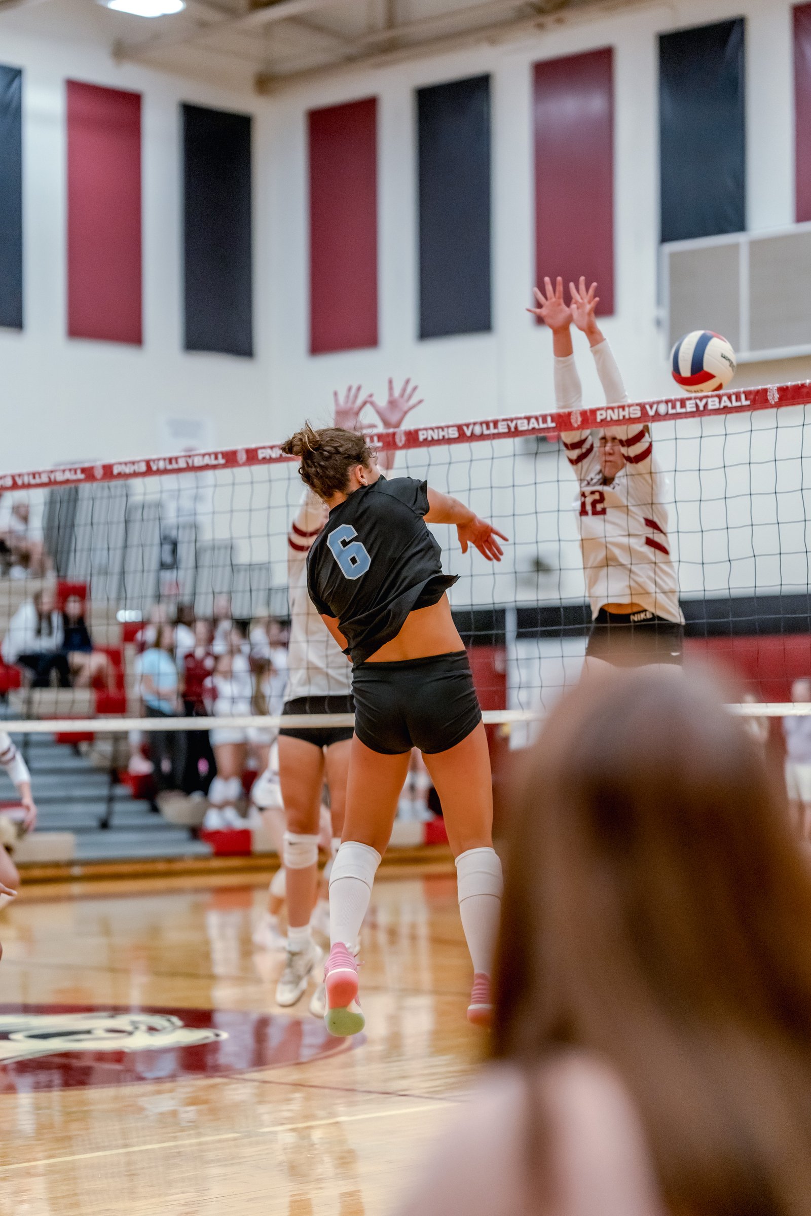 A player in black with jersey number 6 jumps to hit the volleyball, while a player in white with jersey number 12 attempts to block.