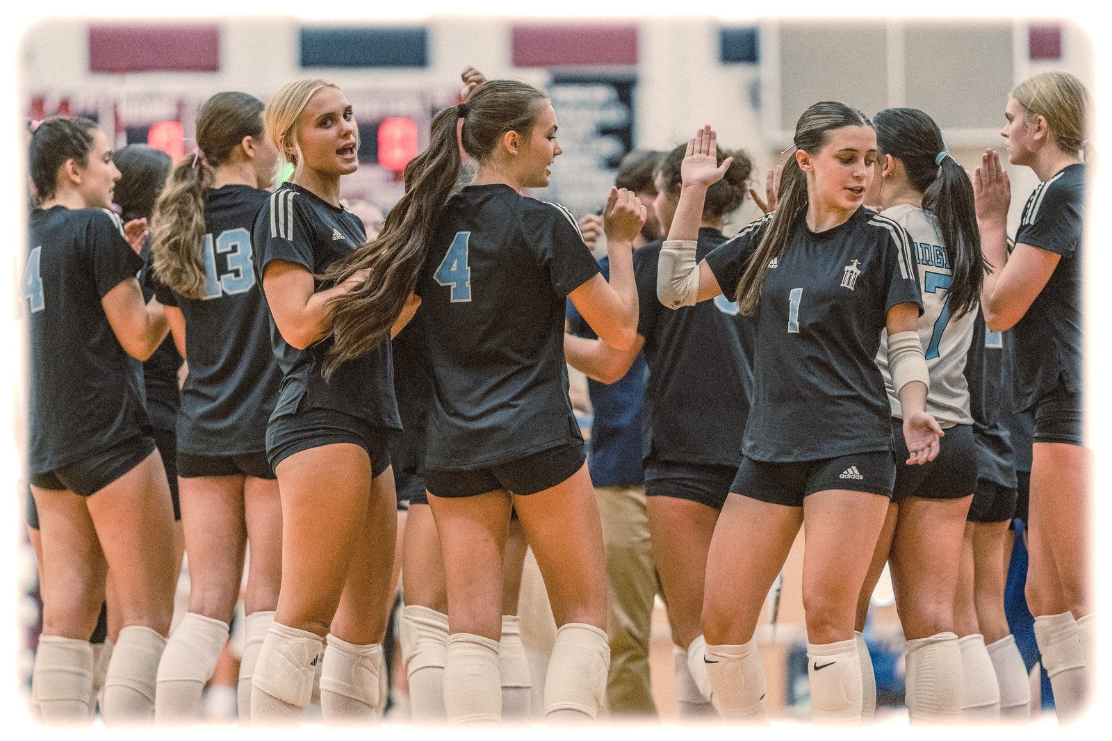 Players in black and light blue jerseys high-five on the court during a volleyball game.