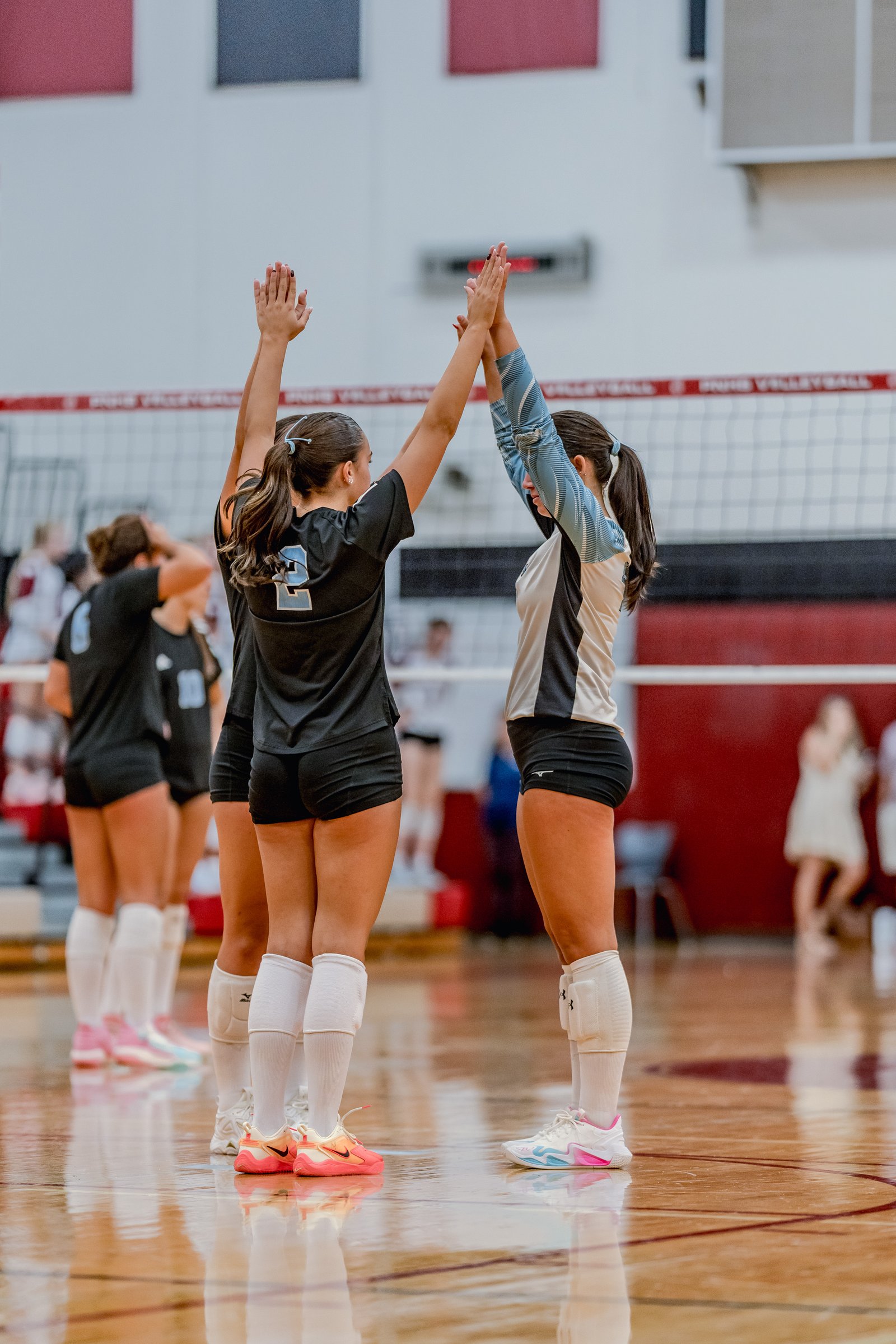 Players in black and blue jerseys high-five on the court during a volleyball game.