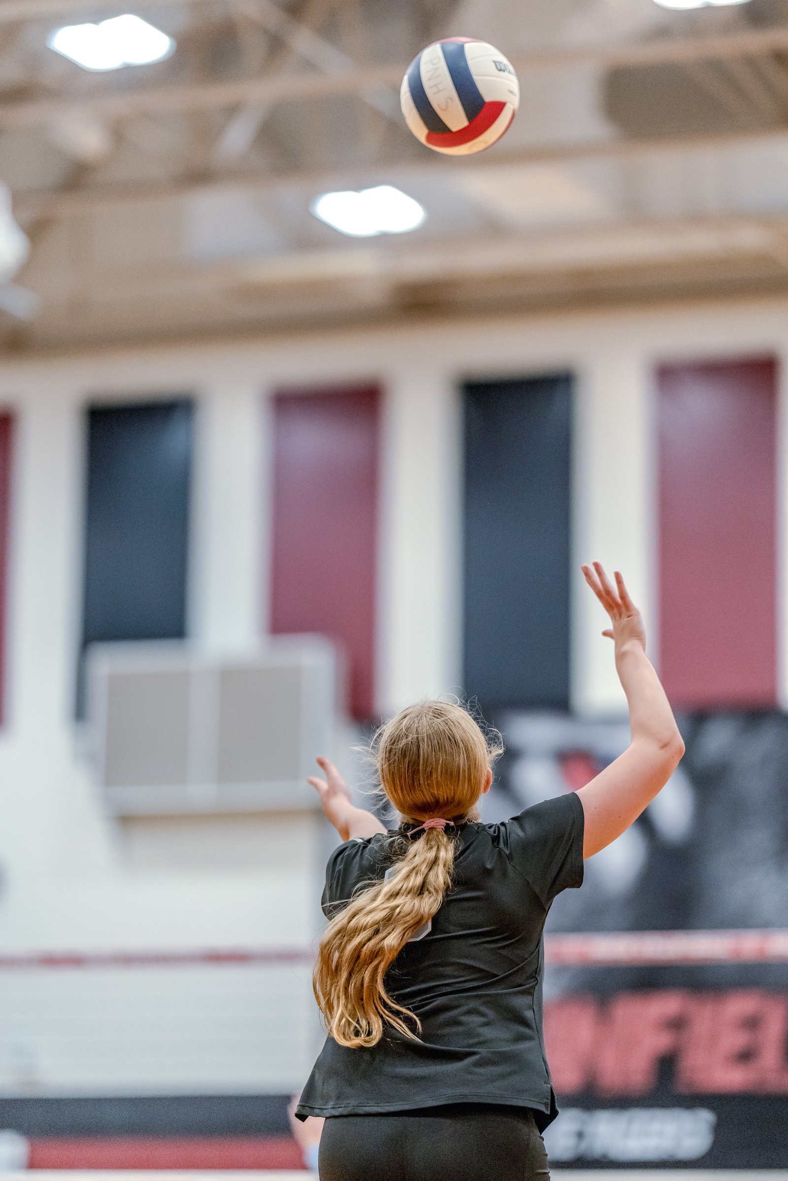 A player in a black top sets the volleyball during a game in a gymnasium.