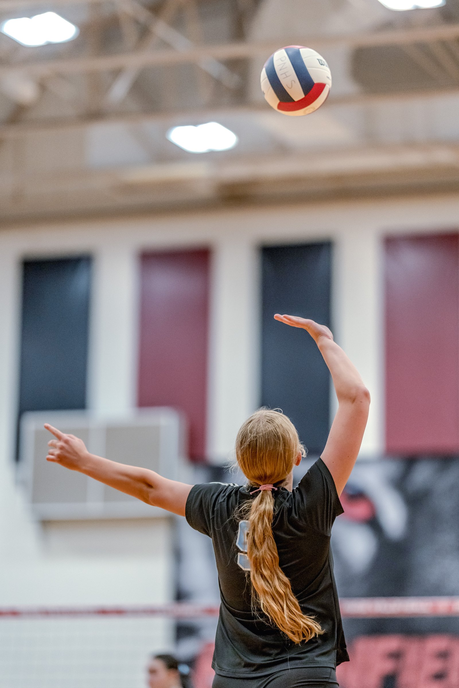 A player in a black jersey with number 9 serves a volleyball during a game.