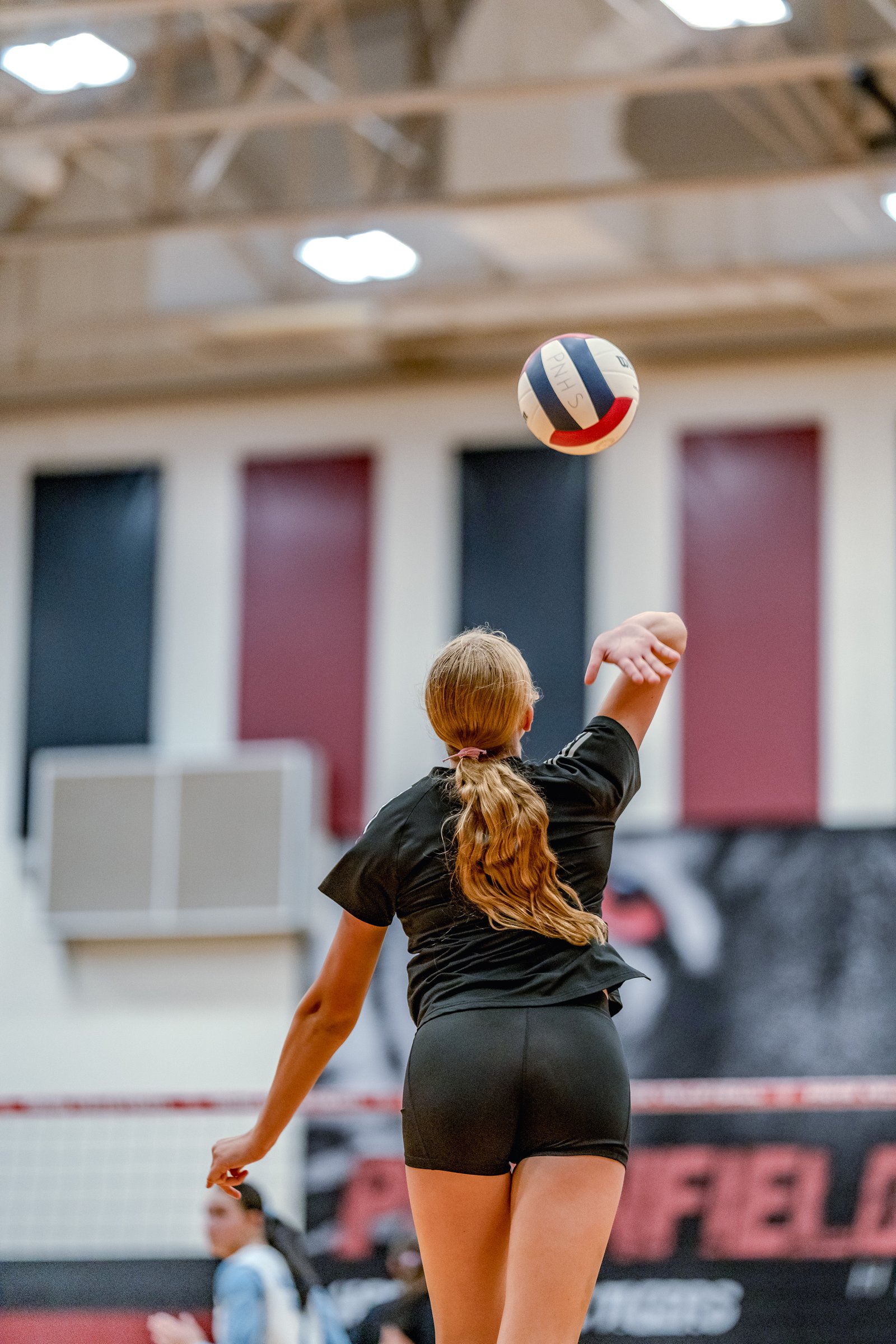 A player in a black top serves a volleyball during a game against PNHS.