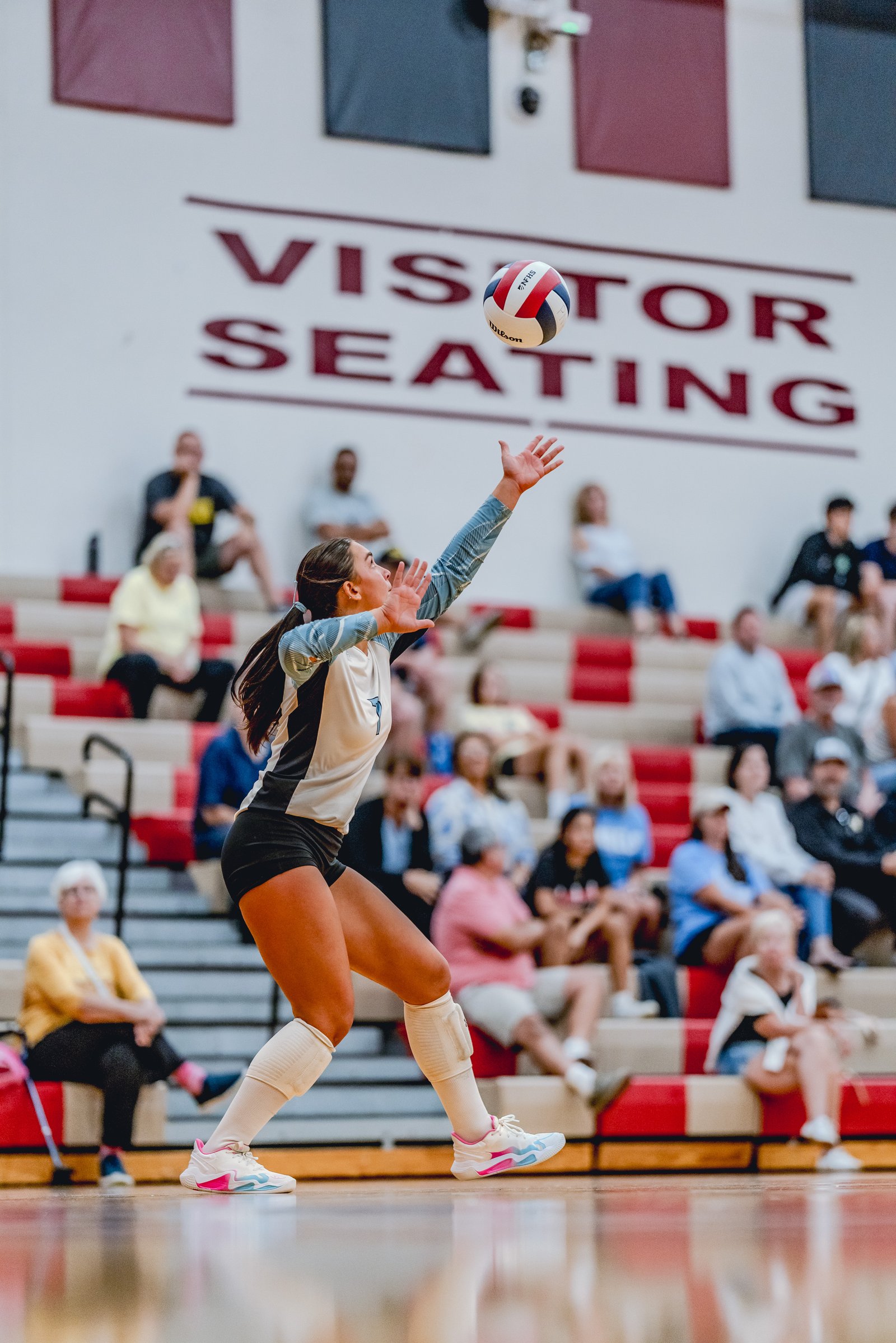A player in a white and black jersey sets the volleyball during a game with spectators in the background.