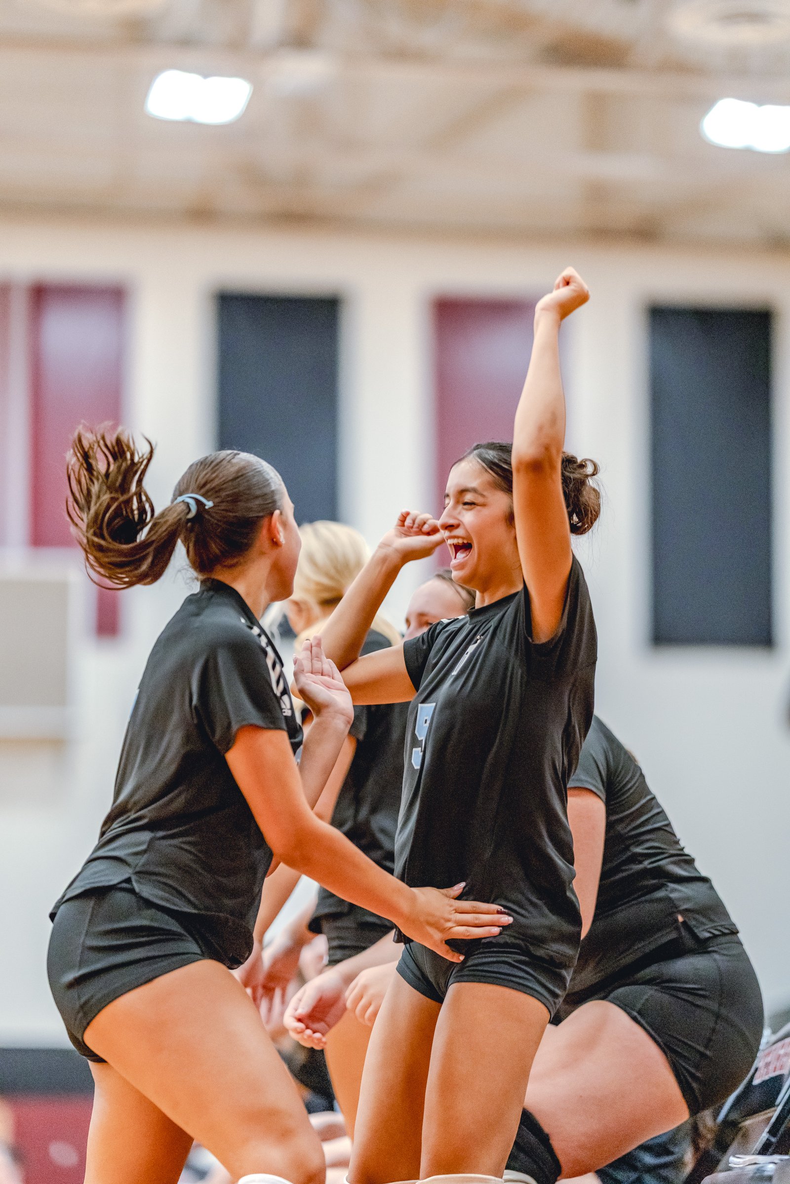 Players in black celebrate with raised arms on the court during a volleyball game.