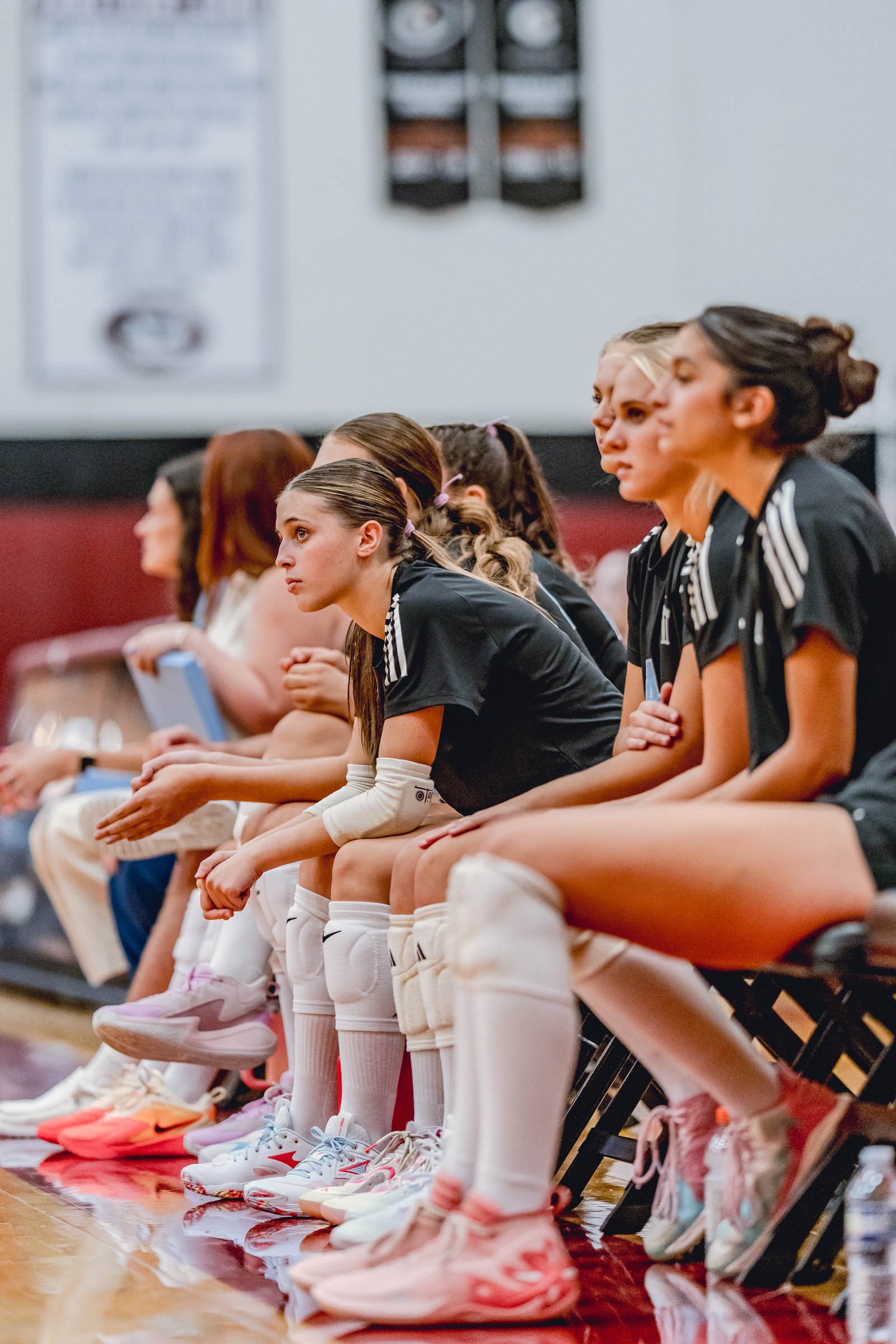Players in black tops and white socks sit on the bench, watching the game.