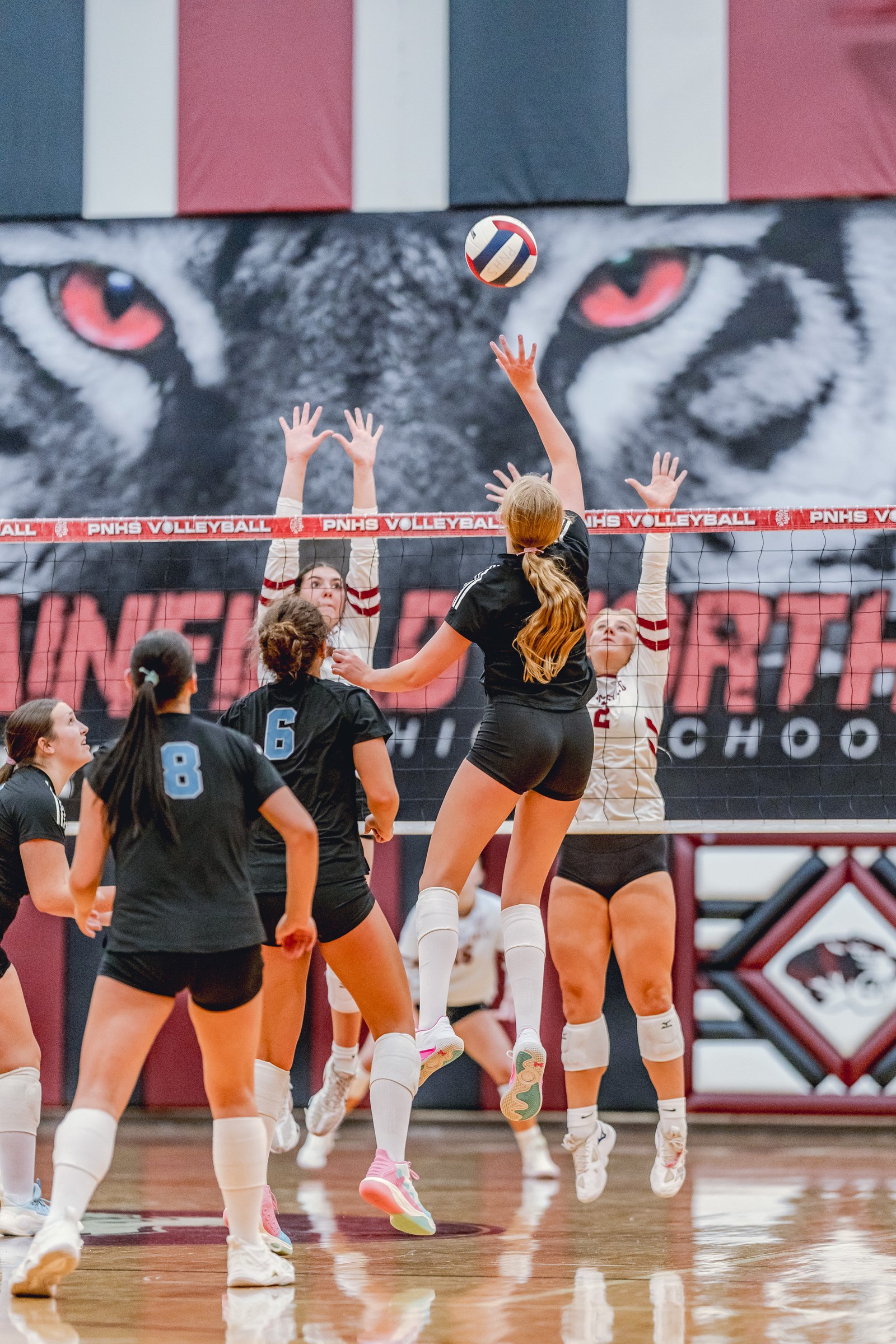 Players in black and white jerseys jump to hit a volleyball over the net during a game.