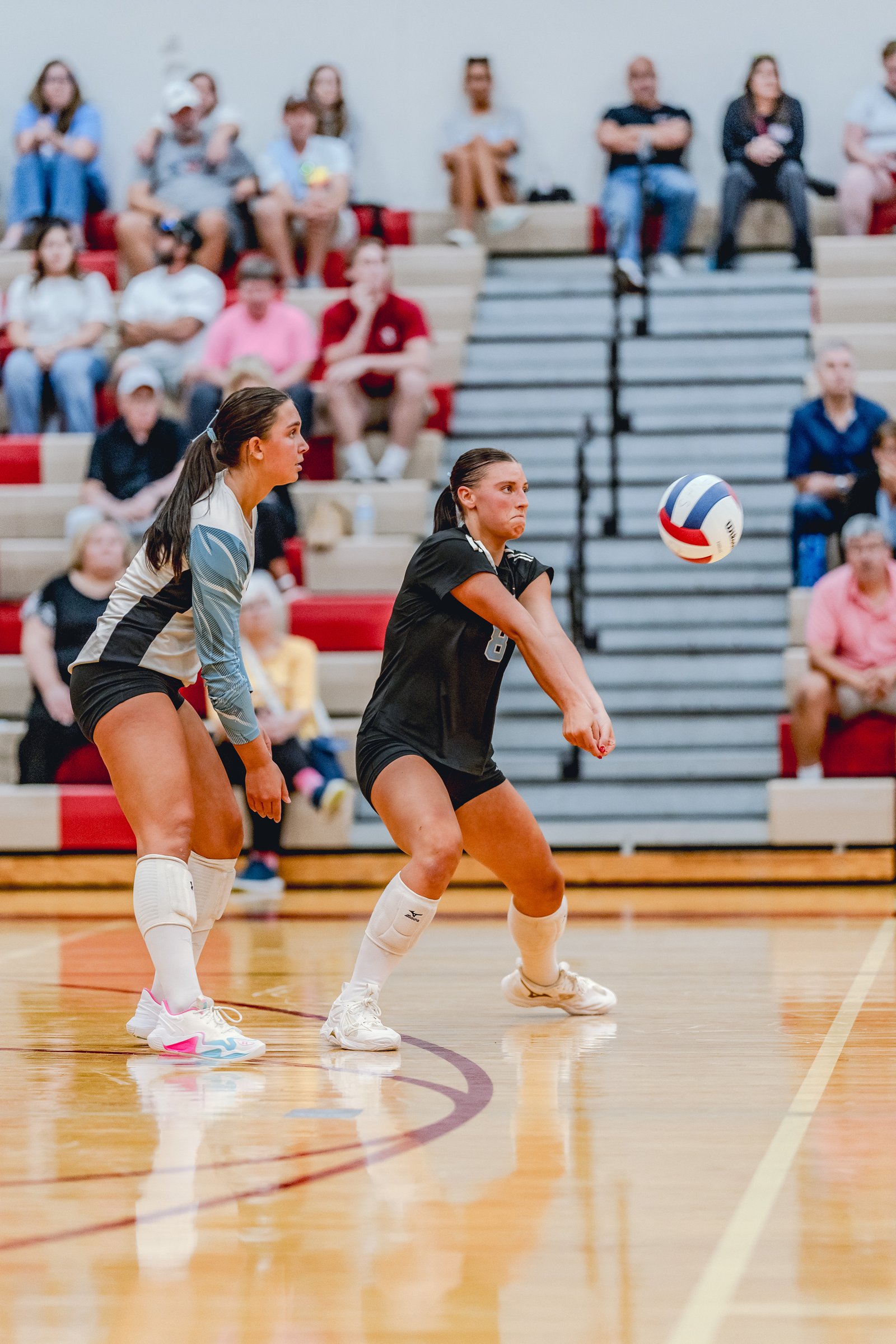 A player in black receives a volleyball as a player in a light blue and black jersey watches.