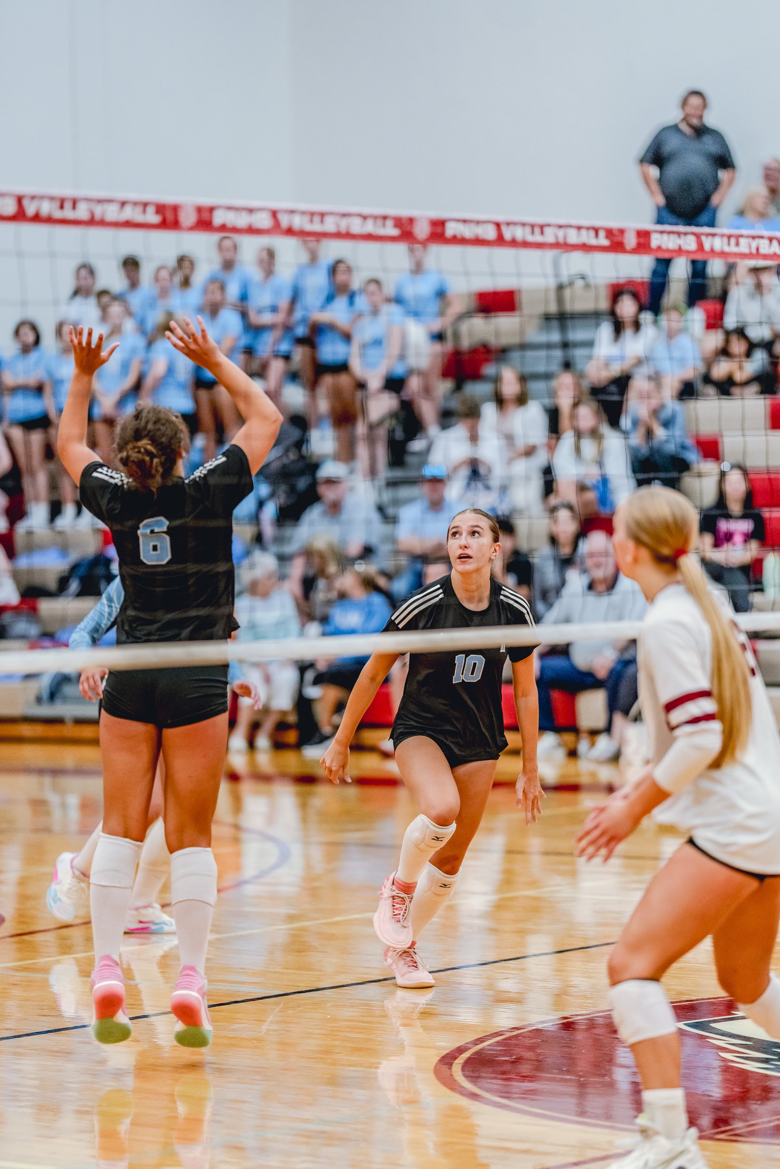 A player in a black top with number 10 jumps as a player in a white top prepares to receive the ball during a volleyball game.