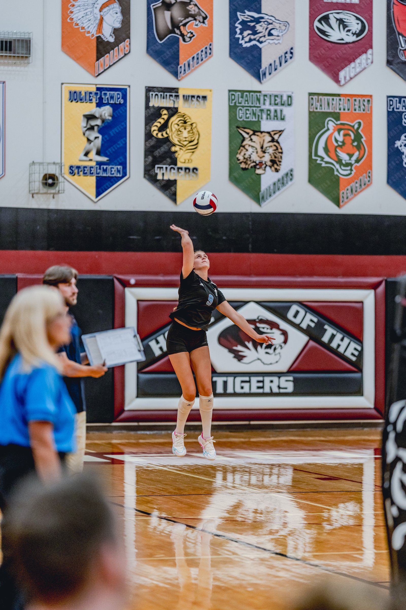 A player in a black top with jersey number 9 serves the volleyball during a game.