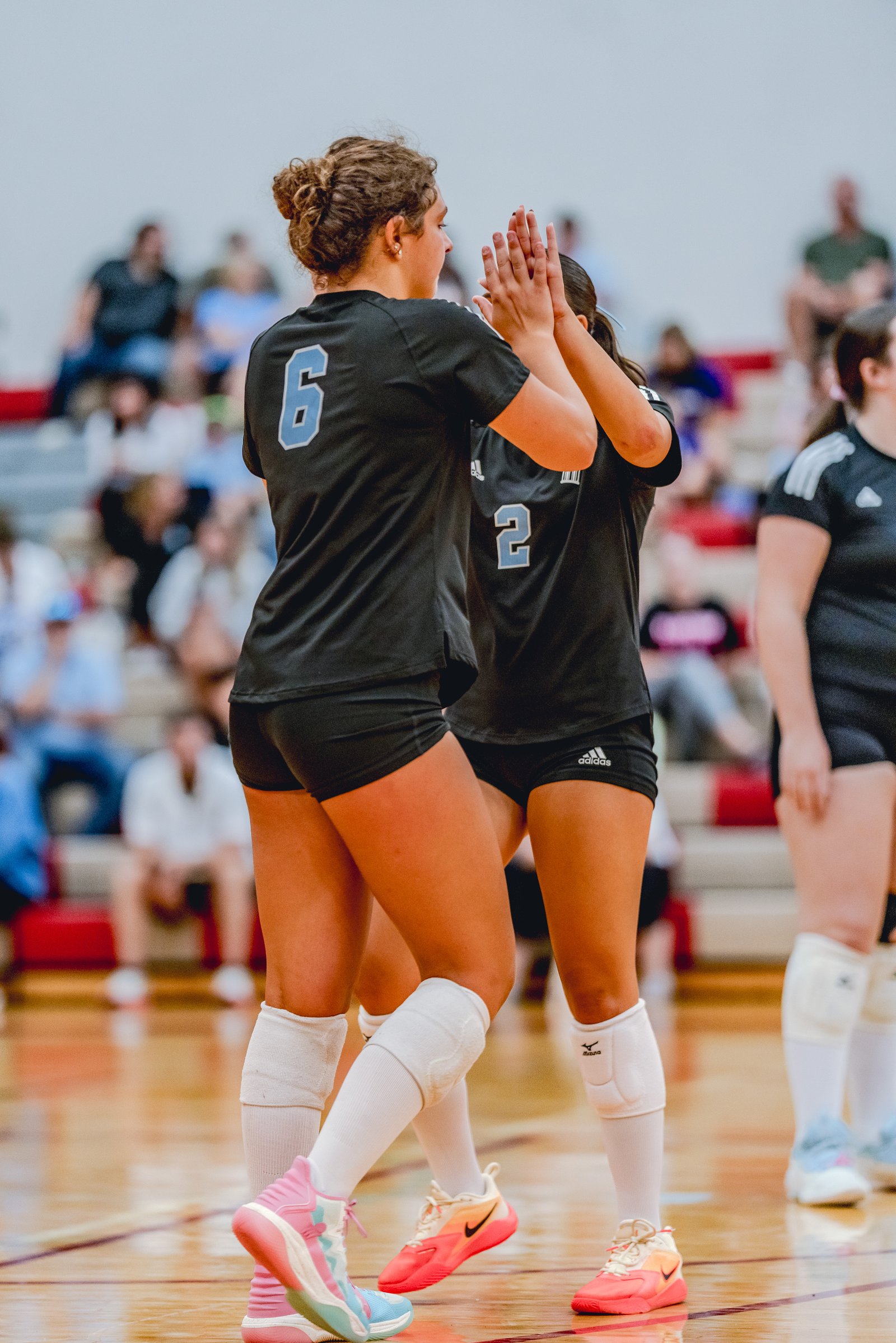 Two players in black jerseys high-five on the court, one wearing number 6 and the other number 2.