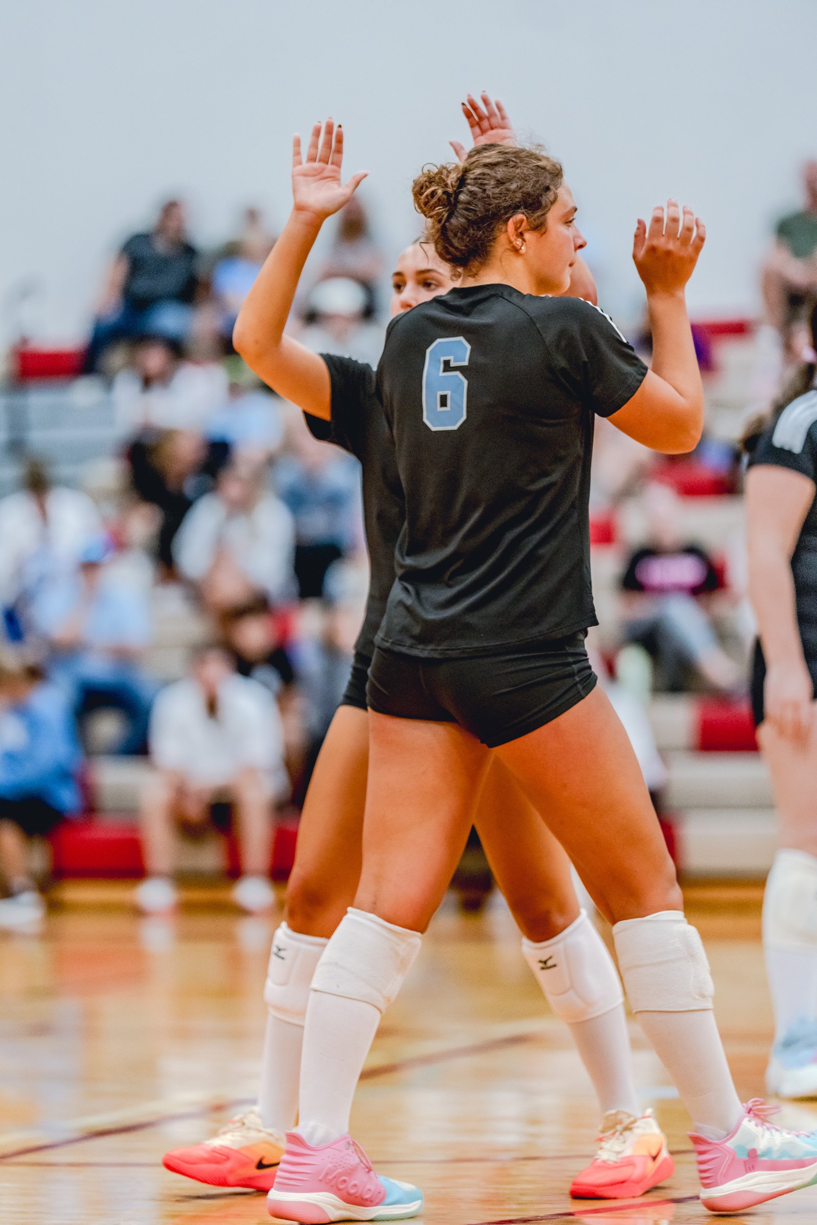 Two players in black tops and white socks high-five on the court, with a player in black jersey number 6 visible.