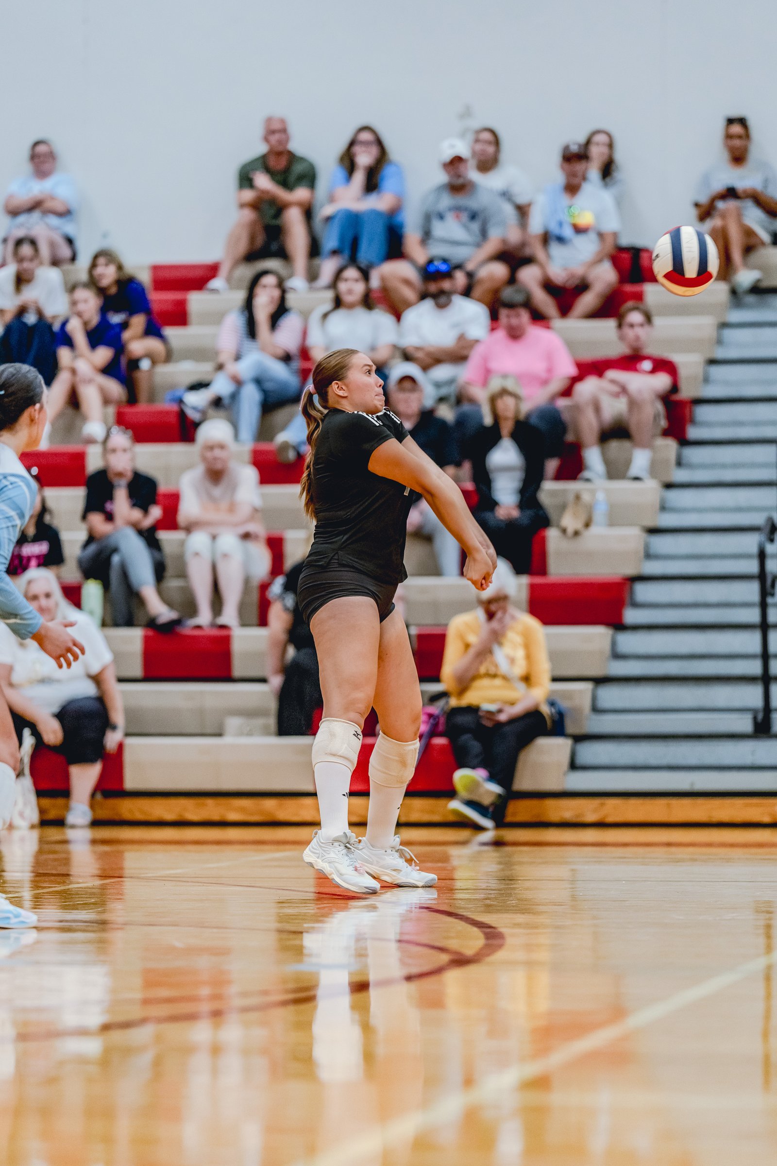 A player in a black top and shorts prepares to hit a volleyball during a game, with spectators in the background.