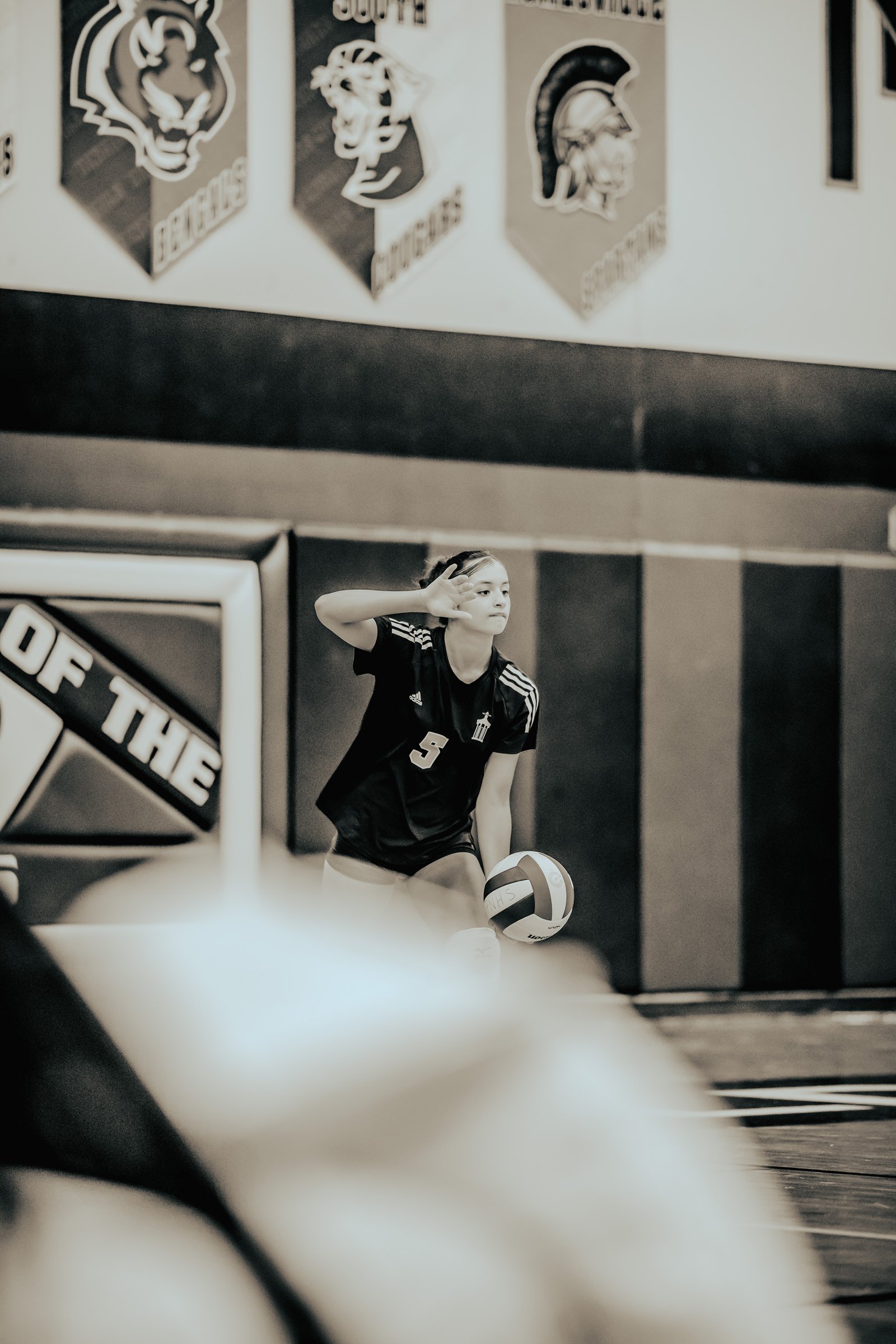 A player in a black jersey with white stripes and number 5 serves a volleyball on the court.